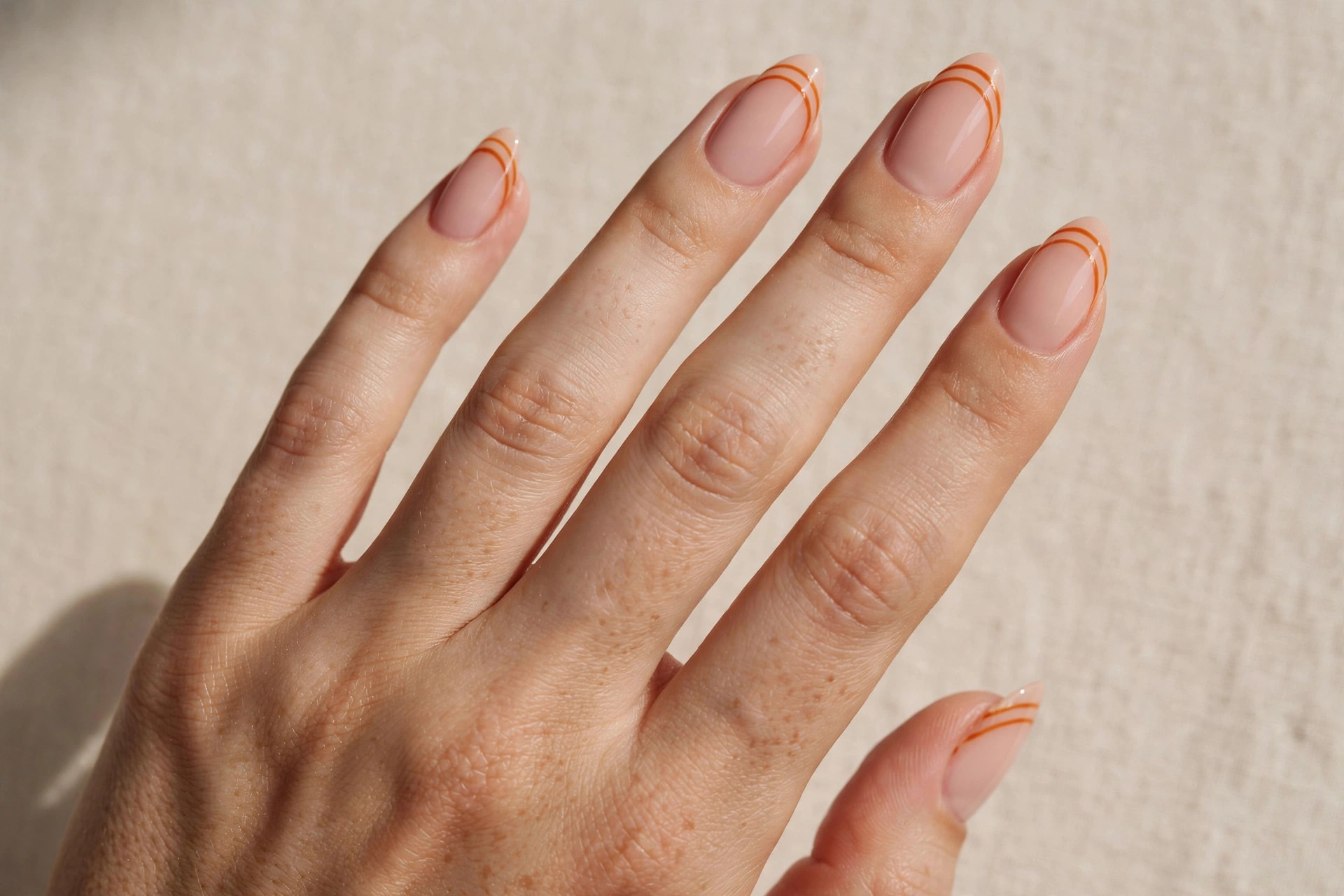 Double French manicure with two thin pumpkin spice orange lines on a nude base