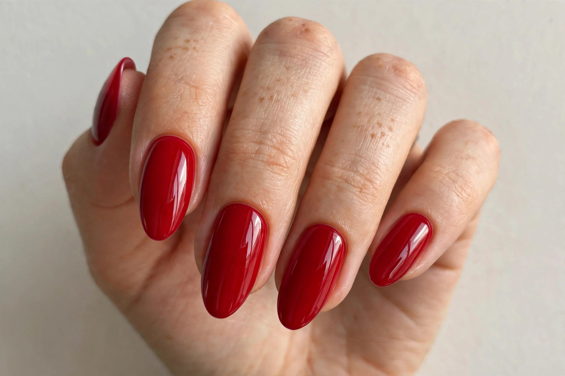 Close-up of a woman's hand with classic glossy red almond-shaped acrylic nails