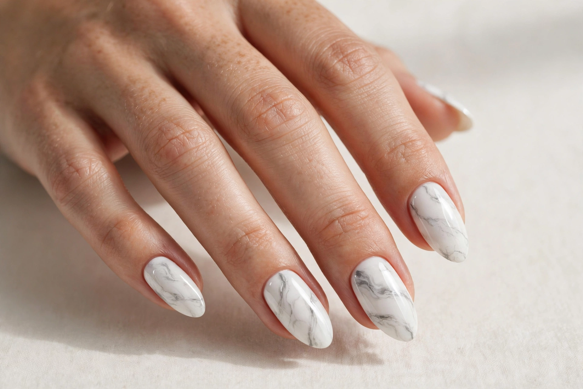 Close-up of a woman's hand with white marble almond-shaped acrylic nails with grey veining