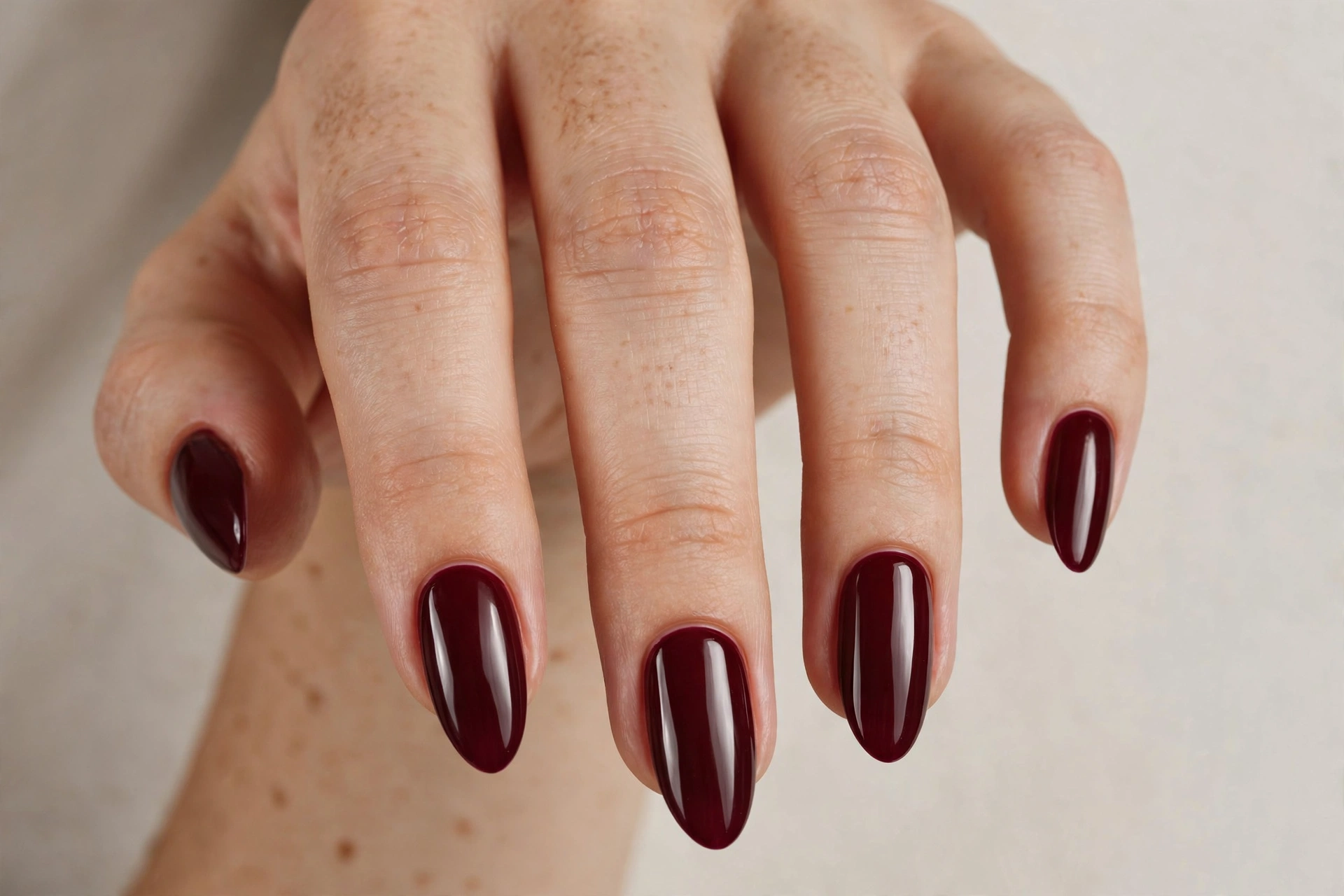 Close-up of a woman's hand with deep burgundy almond-shaped acrylic nails