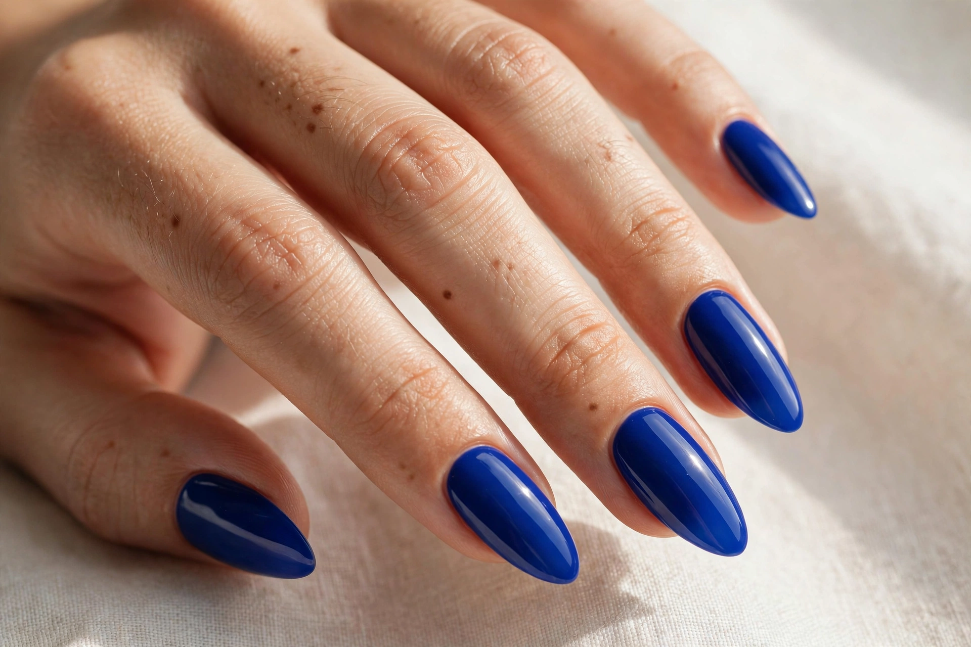 Close-up of a woman's hand with royal blue almond-shaped acrylic nails