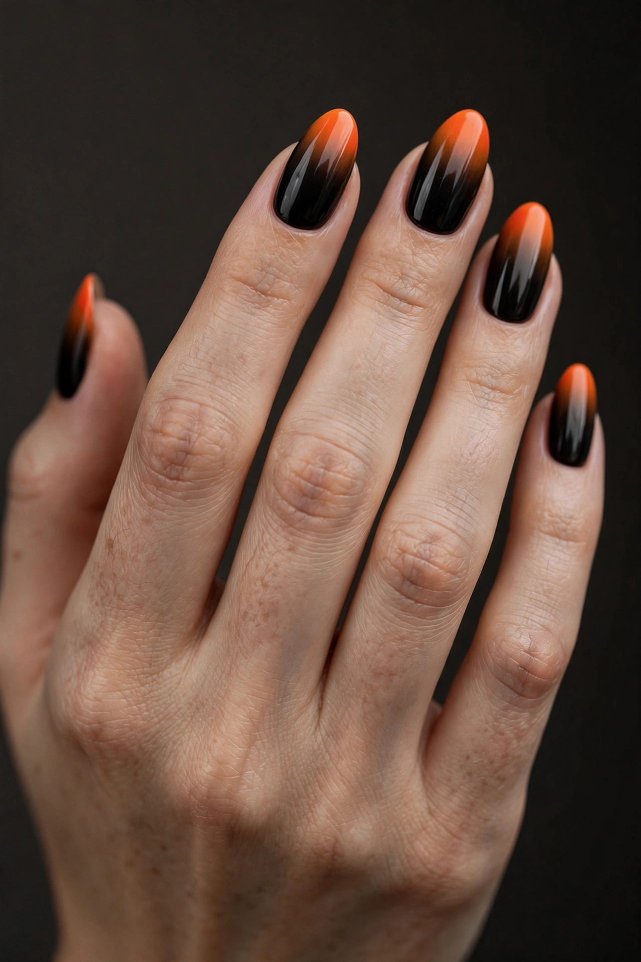 Almond nails with glossy ombré gradient fading from black at the cuticle to vivid orange at the tips