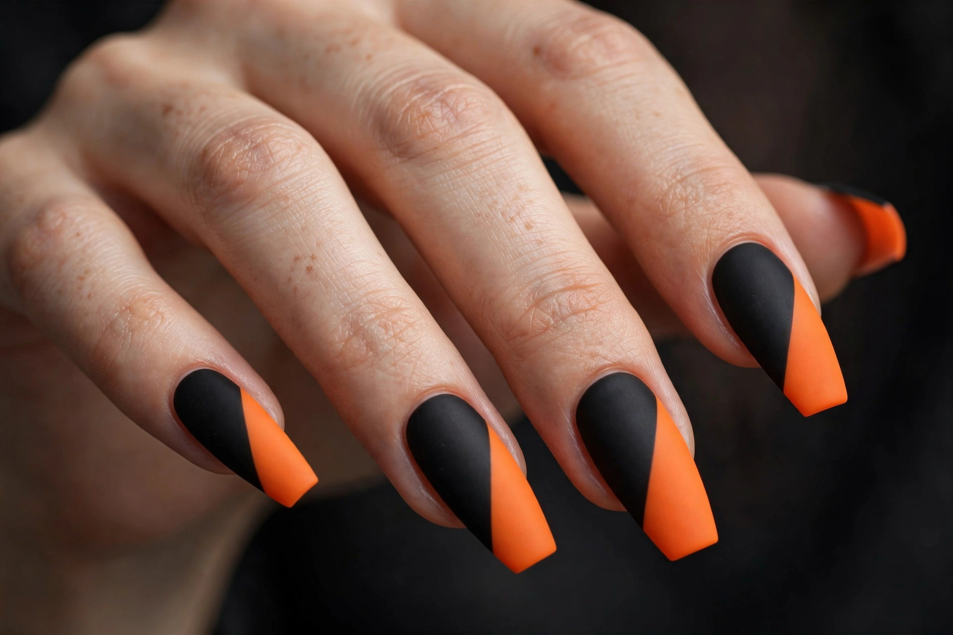 Long coffin nails with bold geometric color-blocking in matte black and bright orange diagonal sections