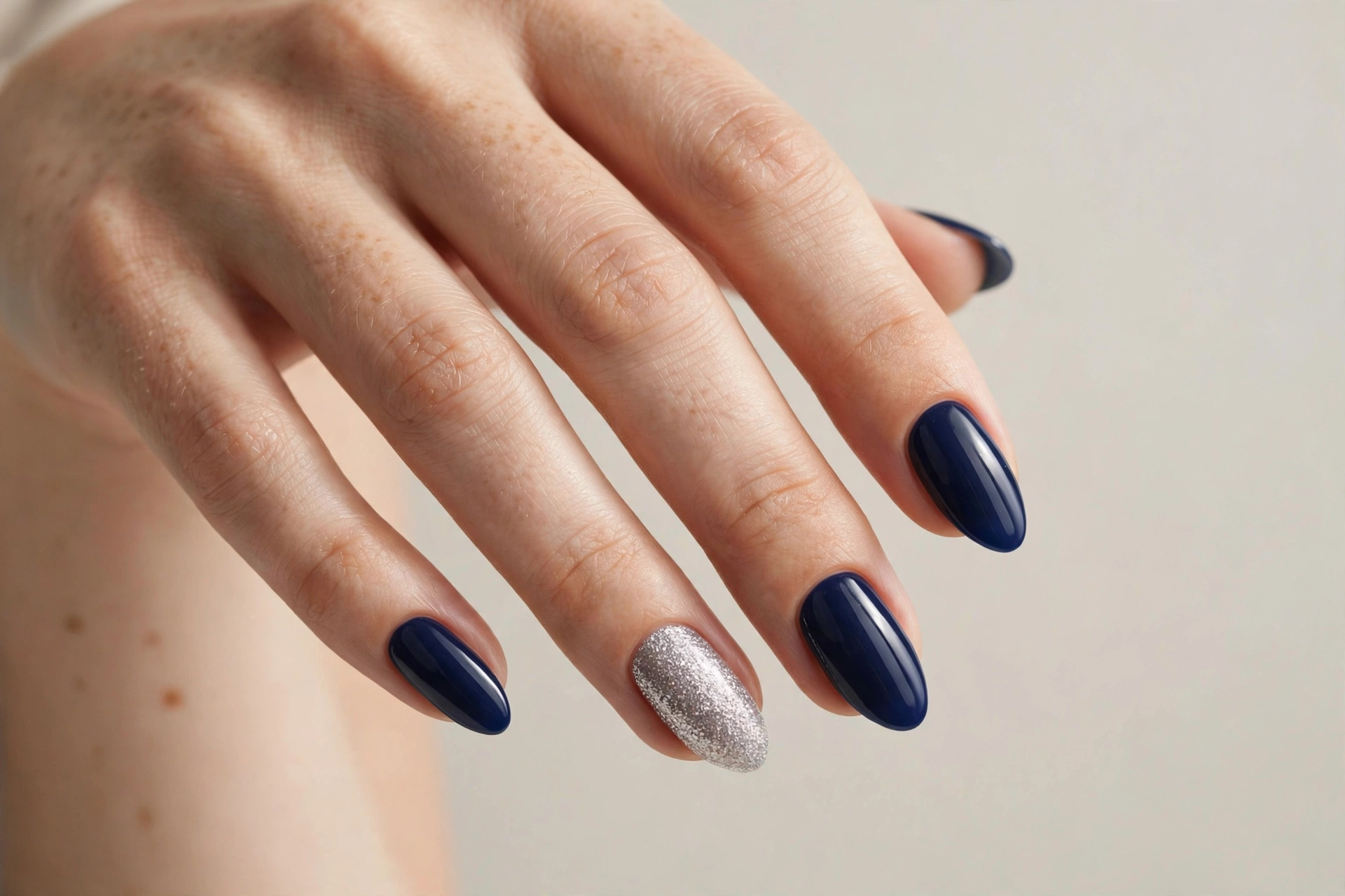 Close-up of a hand with navy blue nails with silver glitter accent nails