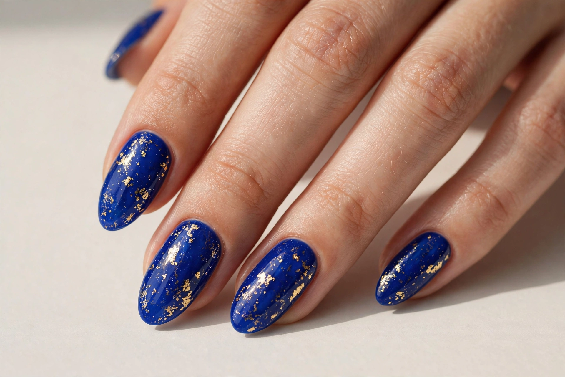 Close-up of a hand with royal blue nails with delicate gold foil flakes