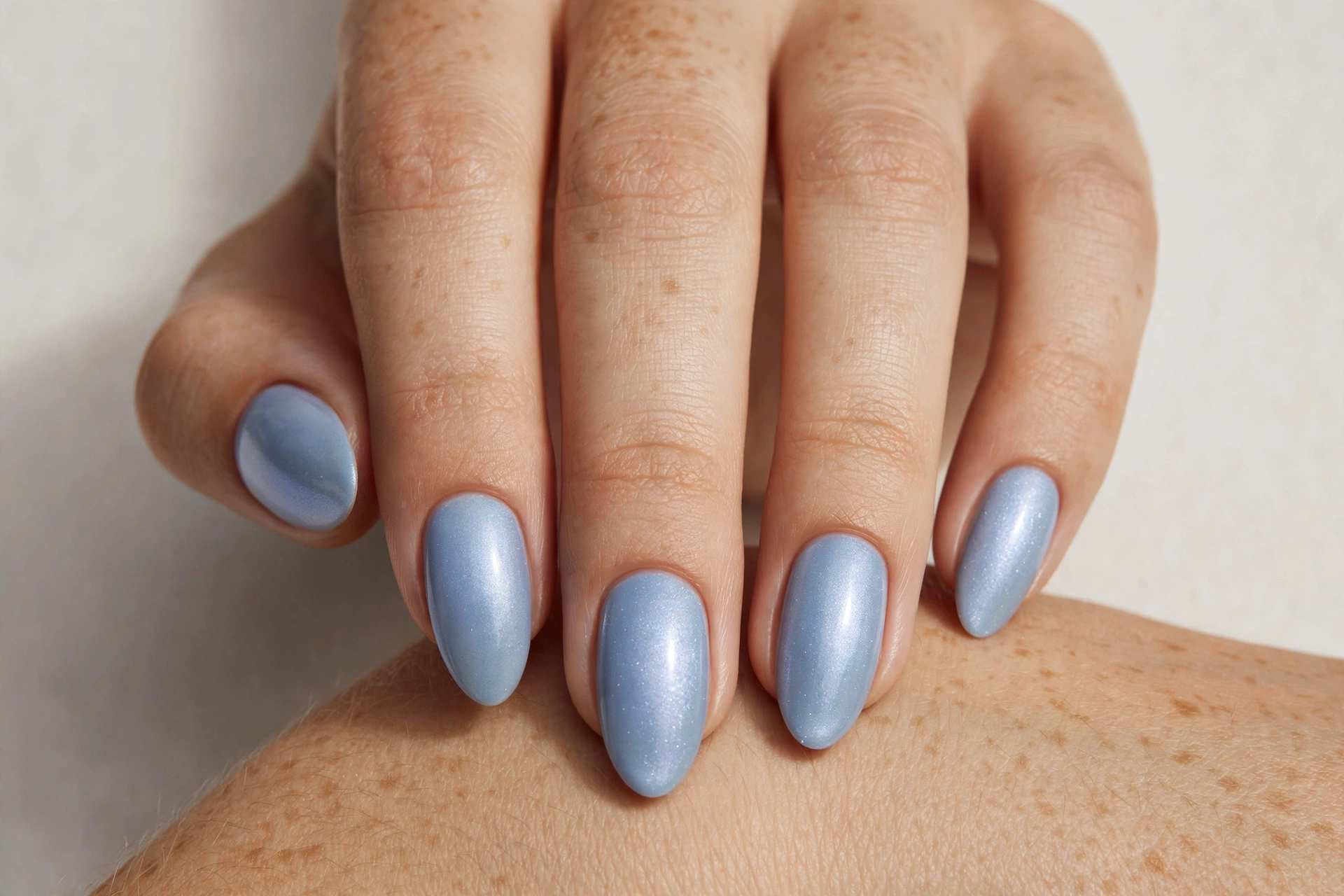 Close-up of a hand with powder blue manicure with soft pearl shimmer finish