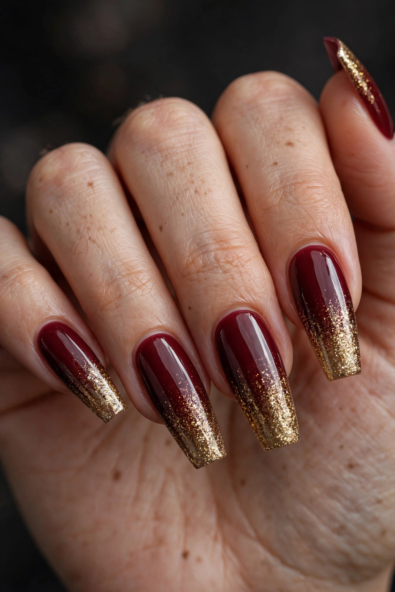 Long coffin nails in deep burgundy polish fading into sparkling gold glitter ombre at the tips