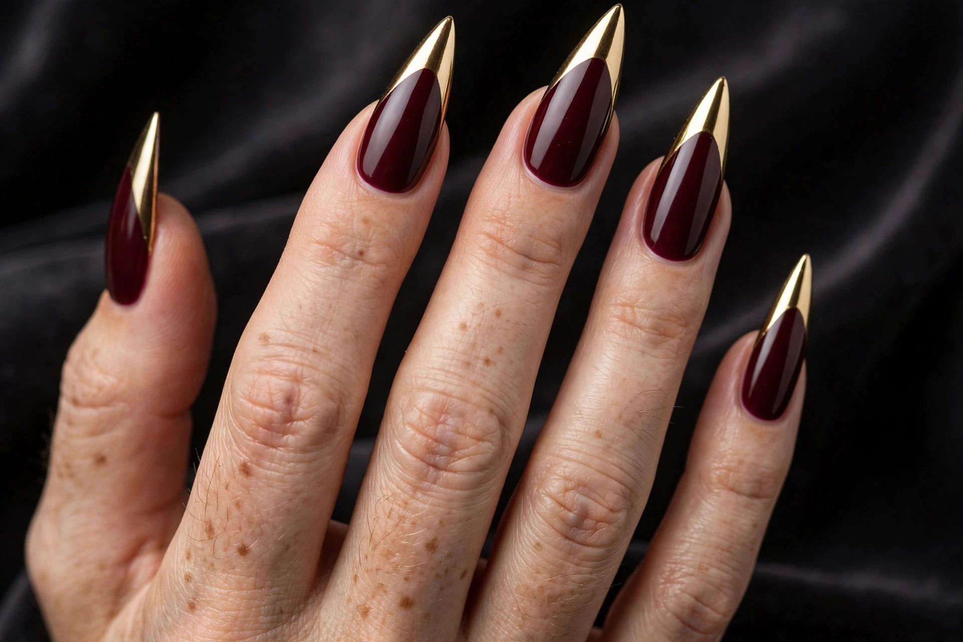 Stiletto nails with deep burgundy base and mirror-shine metallic gold chrome tips