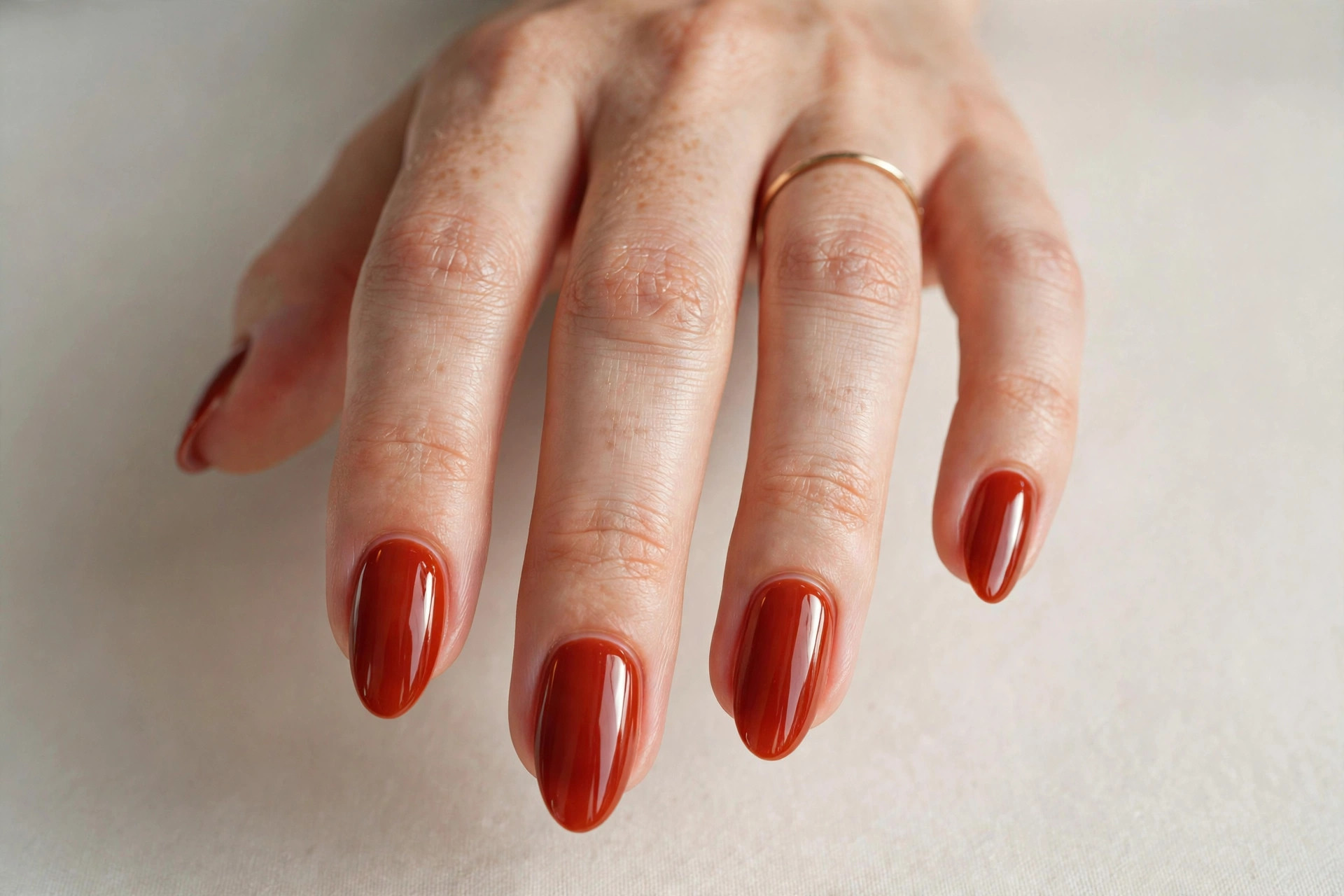 Close-up of a woman's hand with glossy caramel apple red fall manicure on almond shaped nails