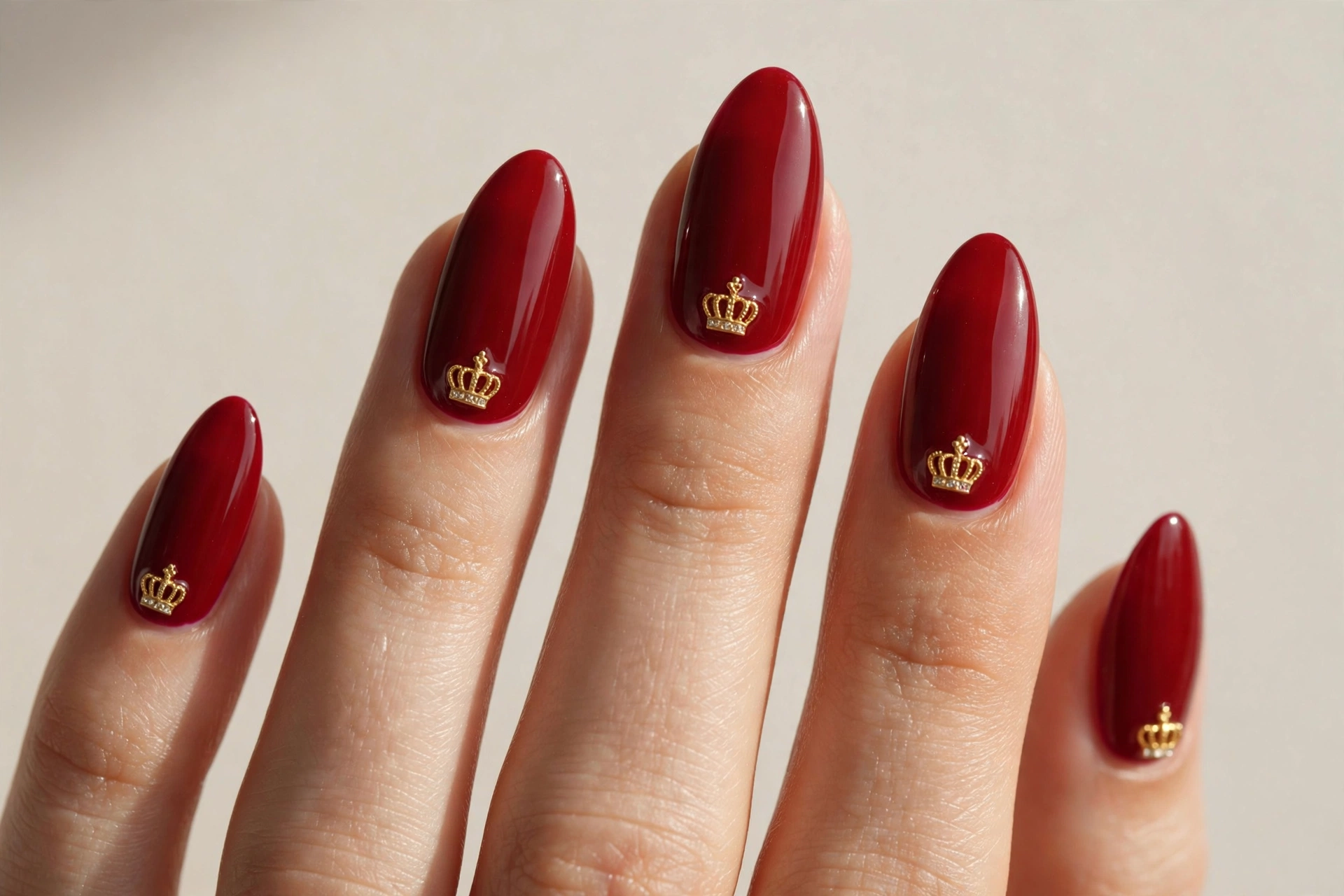 Deep red almond nails with tiny gold crown charms
