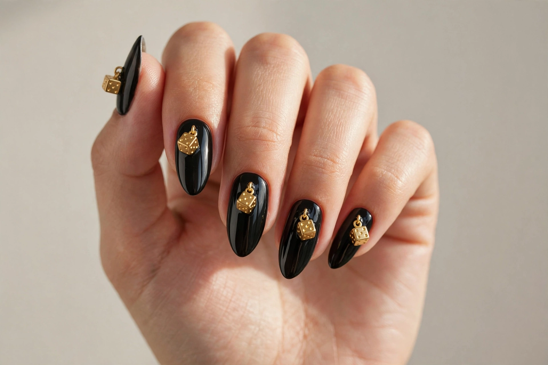 Glossy black almond nails with miniature gold dice charms