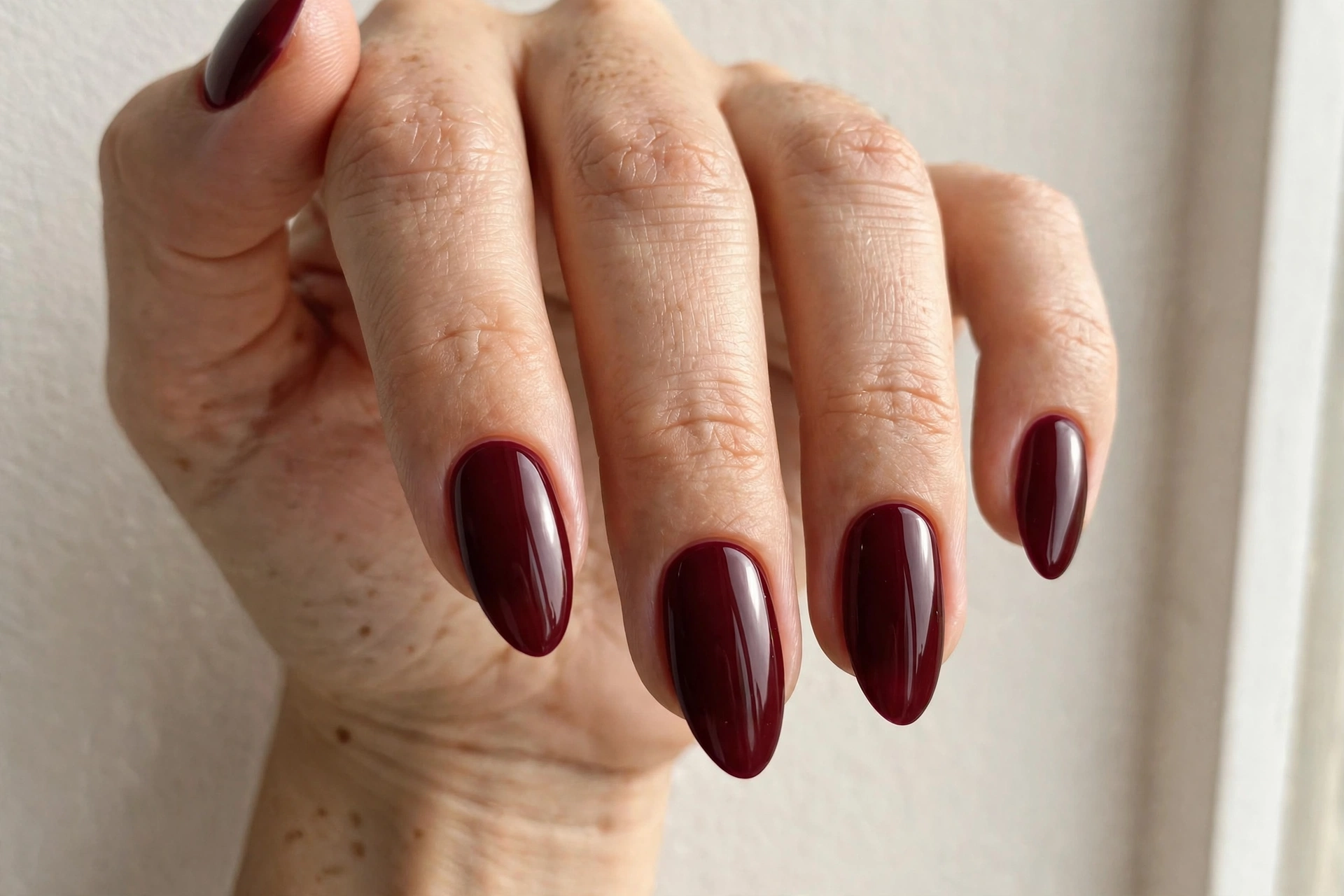 Close-up of a woman's hand with deep burgundy fall manicure on almond shaped nails