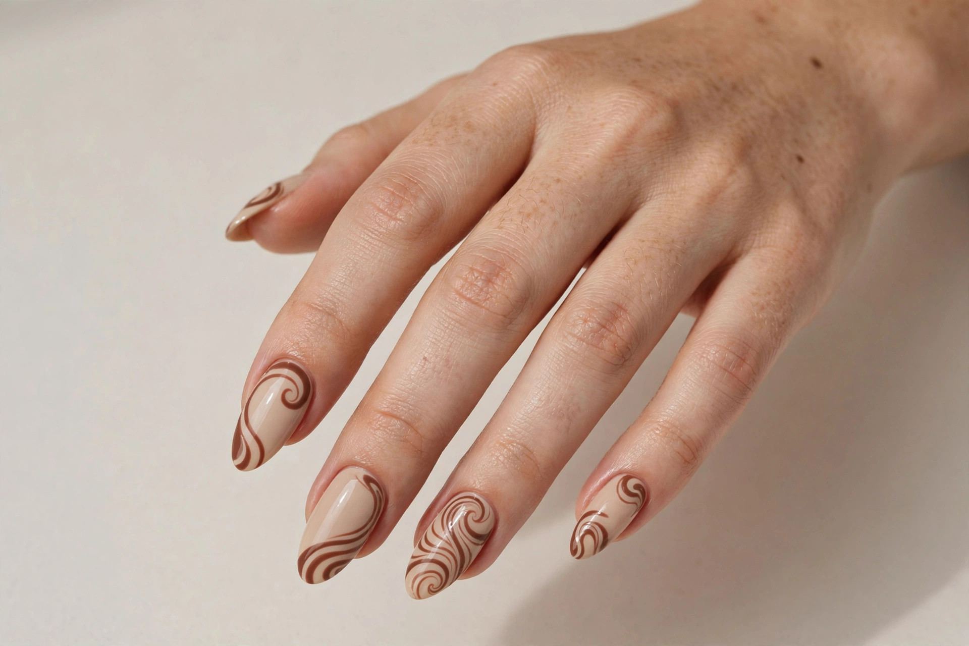 Close-up of a woman's hand with beige manicure and cocoa brown swirl designs