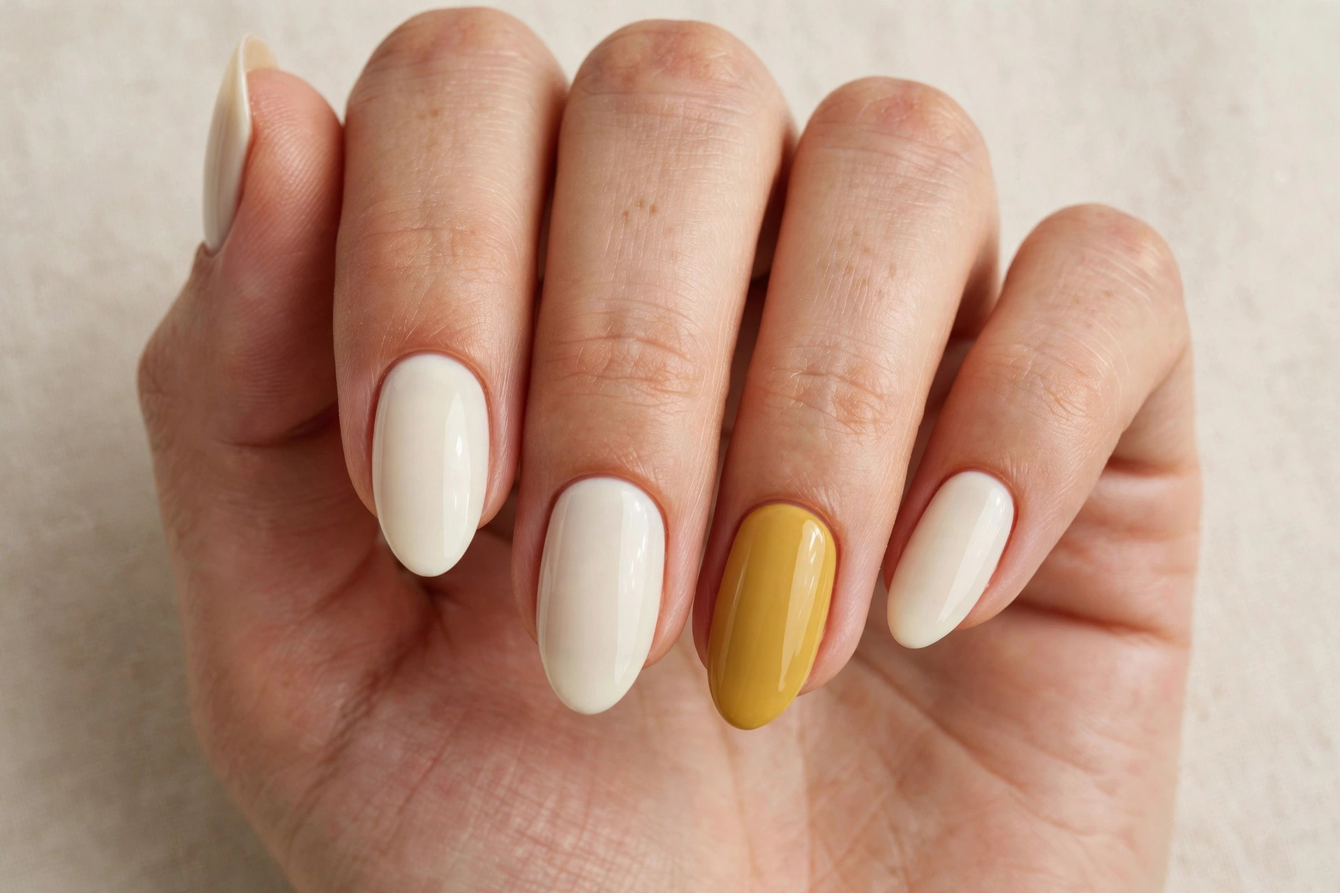 Close-up of a woman's hand with cream manicure and mustard yellow accent nails