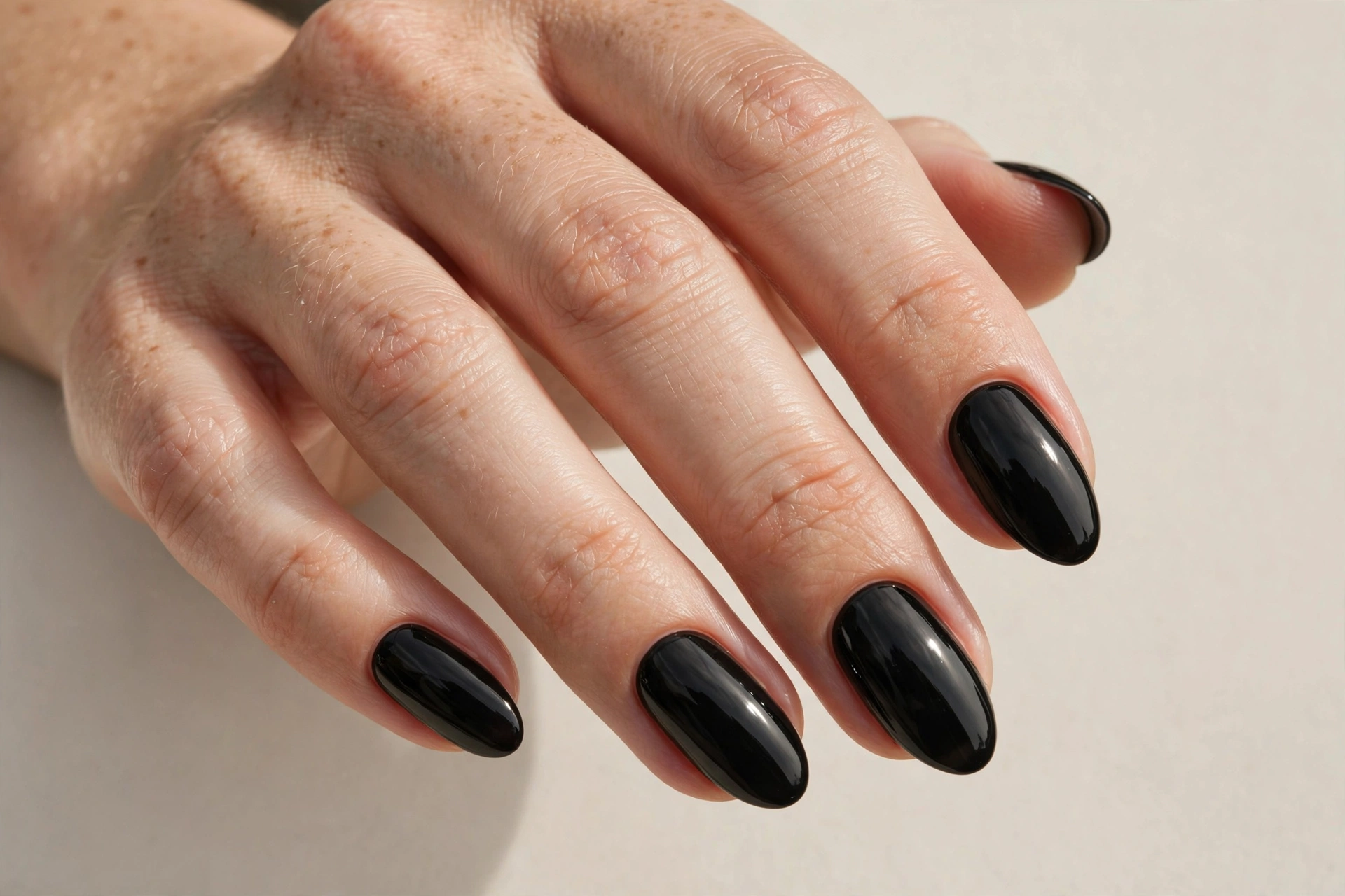 Glossy jet black manicure with high-shine finish on almond shaped nails