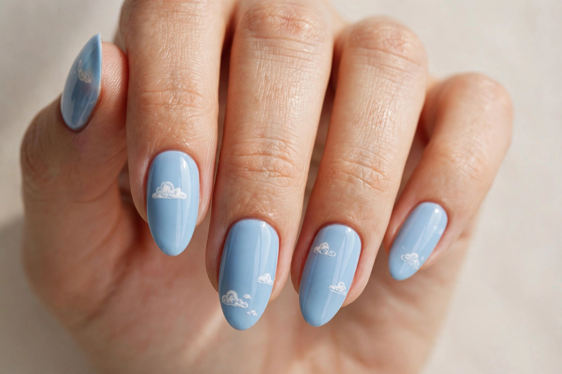 Close-up of baby blue manicure with tiny white cloud nail art on almond shaped nails