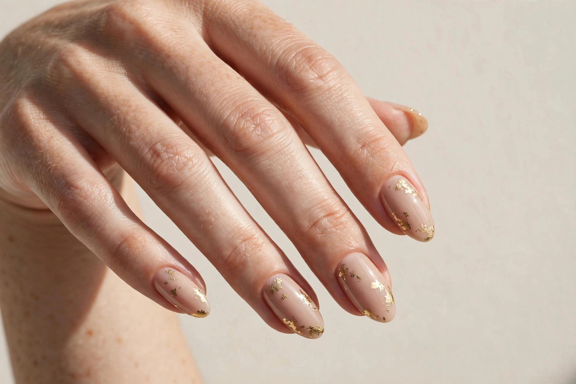 Close-up of soft nude manicure with delicate gold foil flakes on almond shaped nails