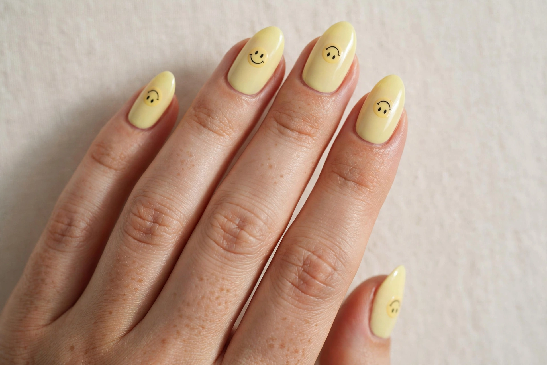 Mini smiley faces on pastel yellow short nails