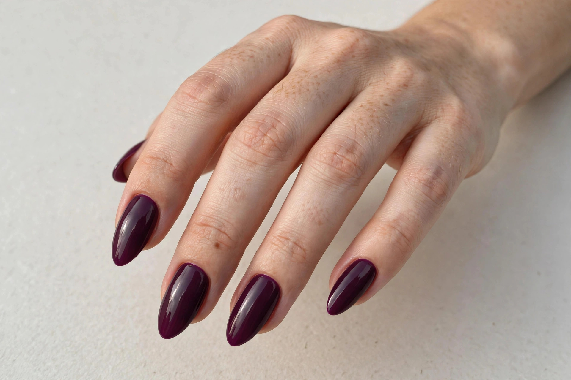 Close-up of a woman's hand with deep plum fall manicure on almond shaped nails