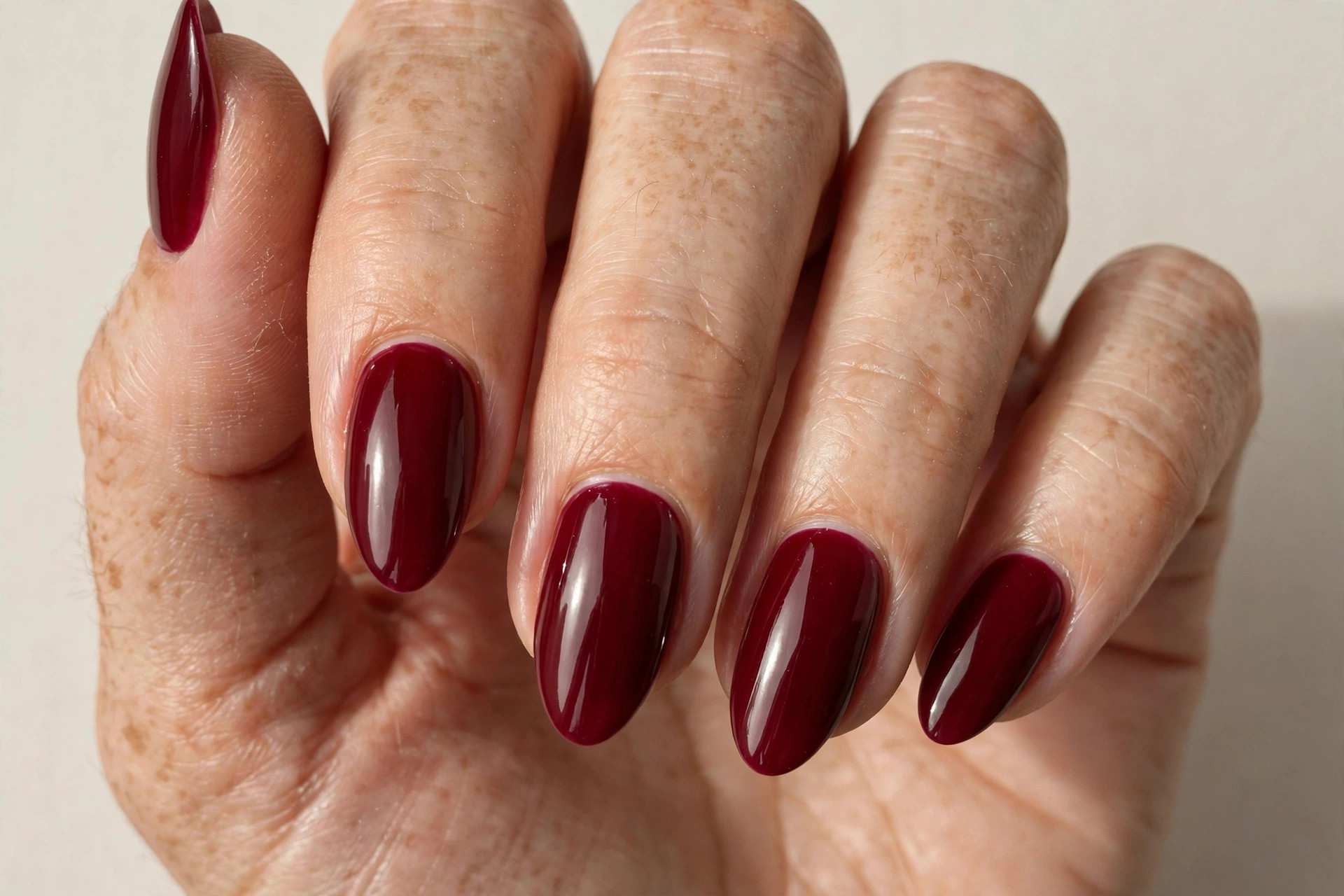 Deep burgundy red almond-shaped nails with glossy finish