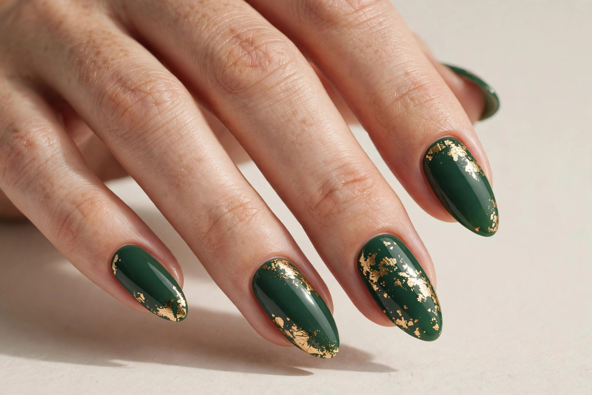 Close-up of a woman's hand with forest green nails and gold foil accents