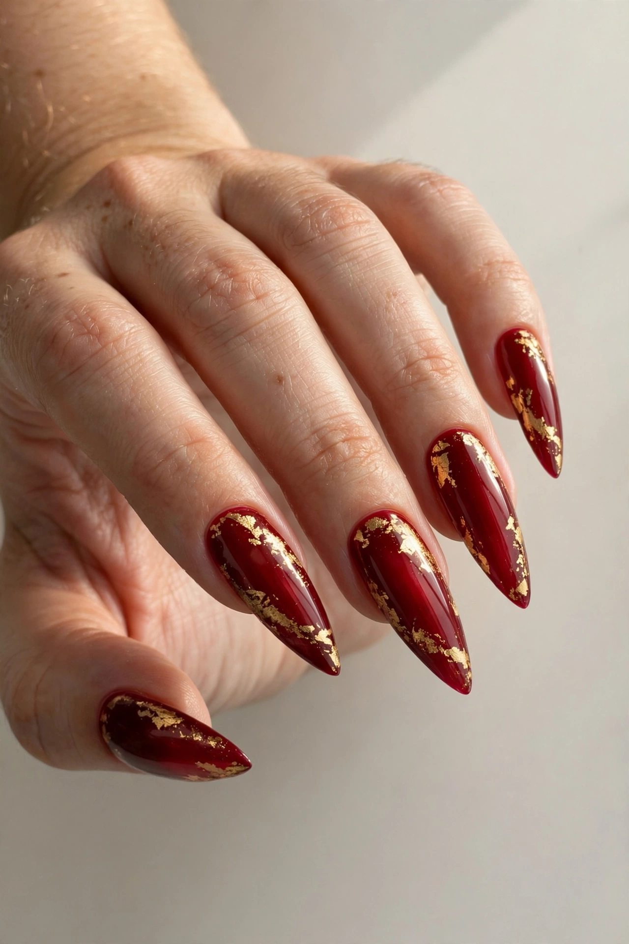Deep red stiletto nails with delicate gold foil accents