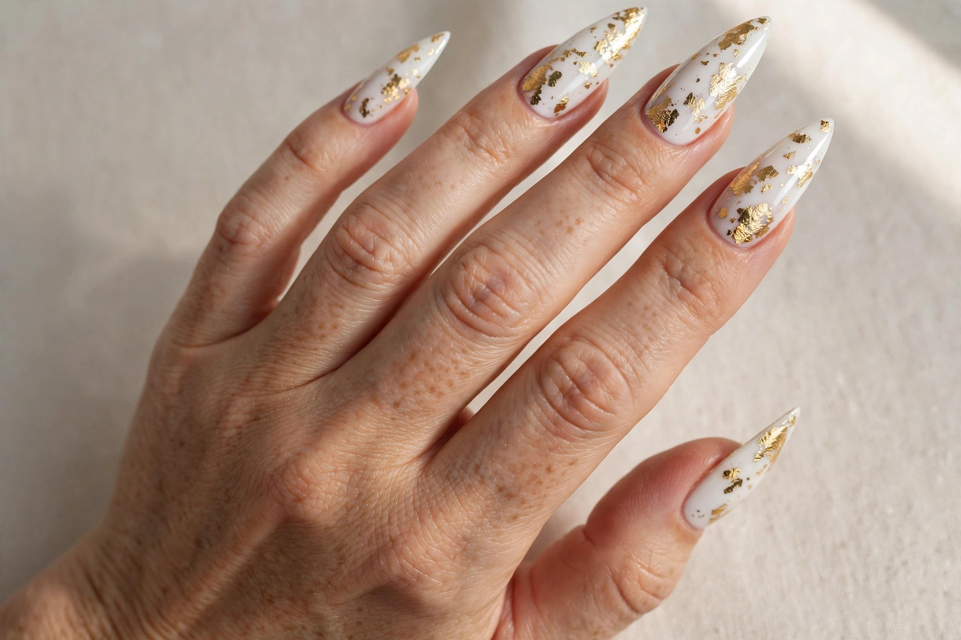 White stiletto nails decorated with gold foil flakes