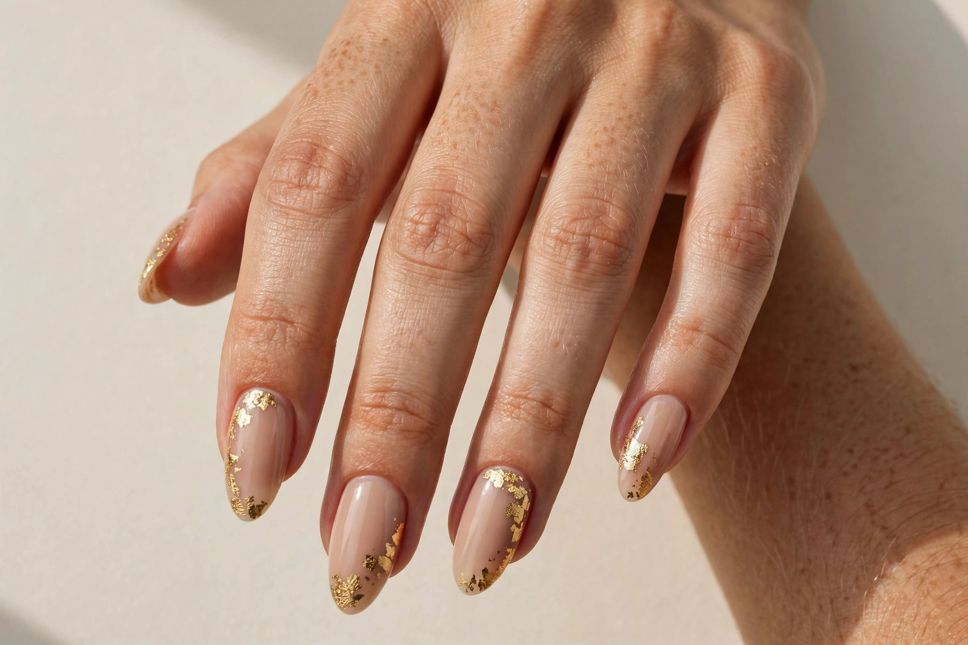 Nude almond nails decorated with delicate gold leaf flakes