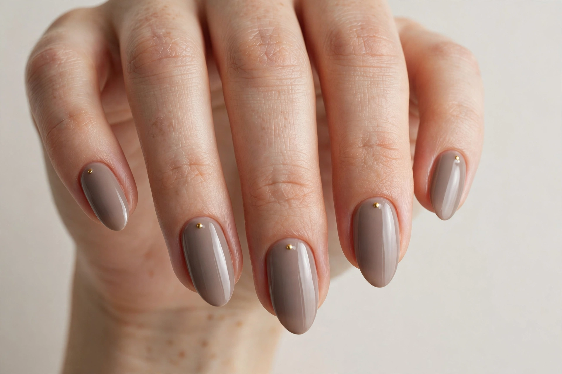 Taupe almond nails with a single tiny gold dot near the cuticle