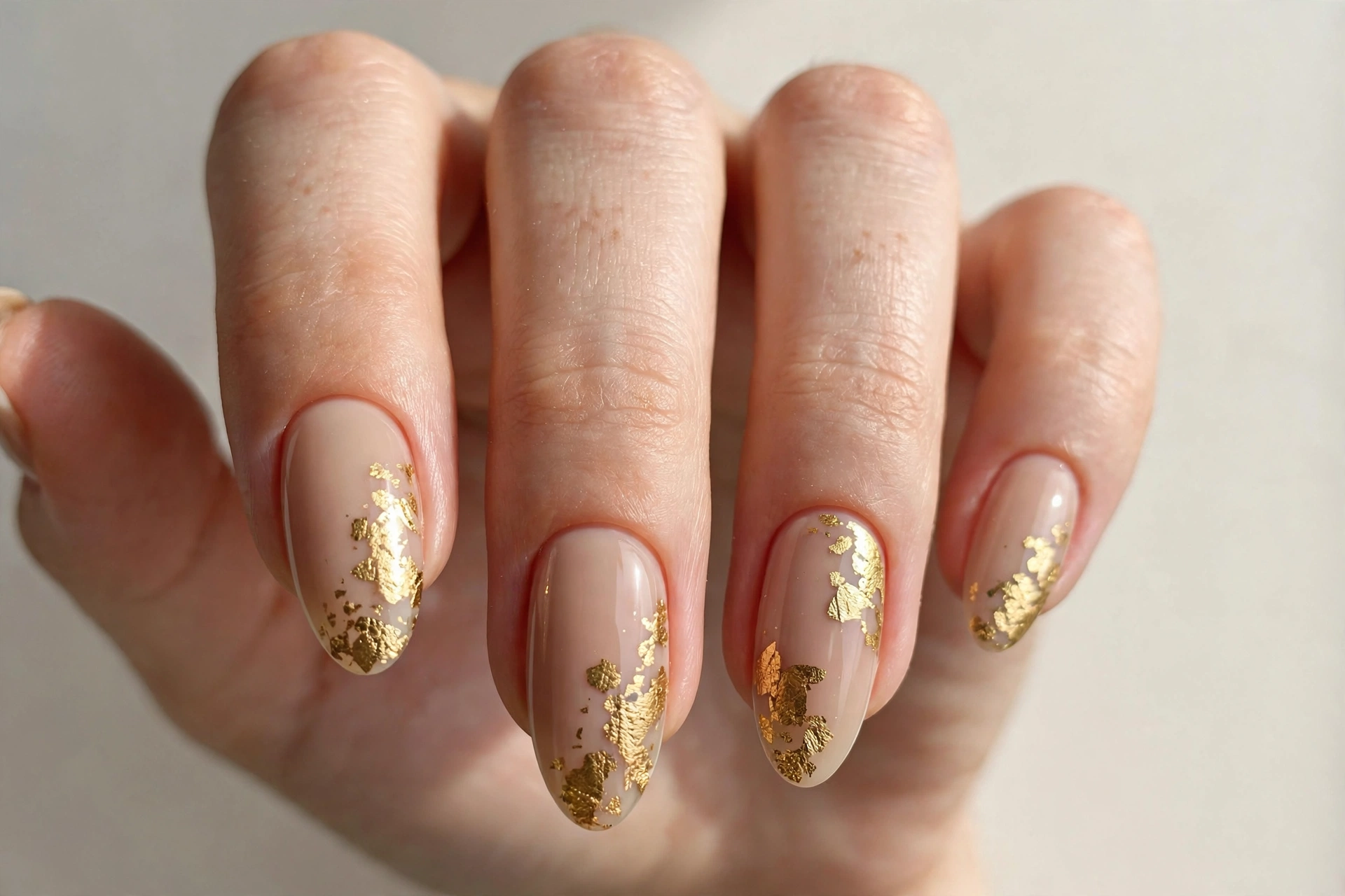 Gold foil flakes on nude almond shaped nails