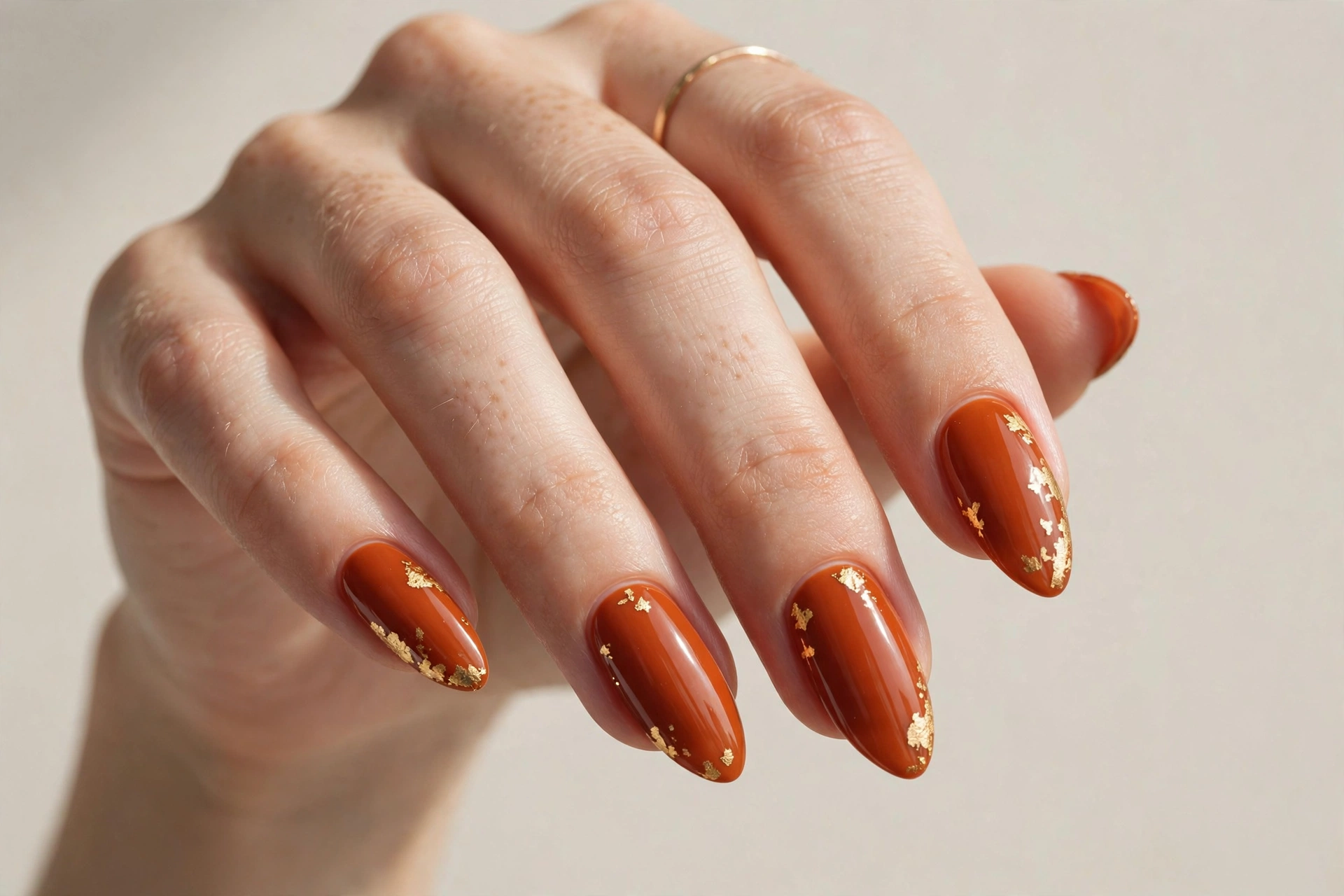 Burnt orange nails with gold foil accents on almond-shaped nails