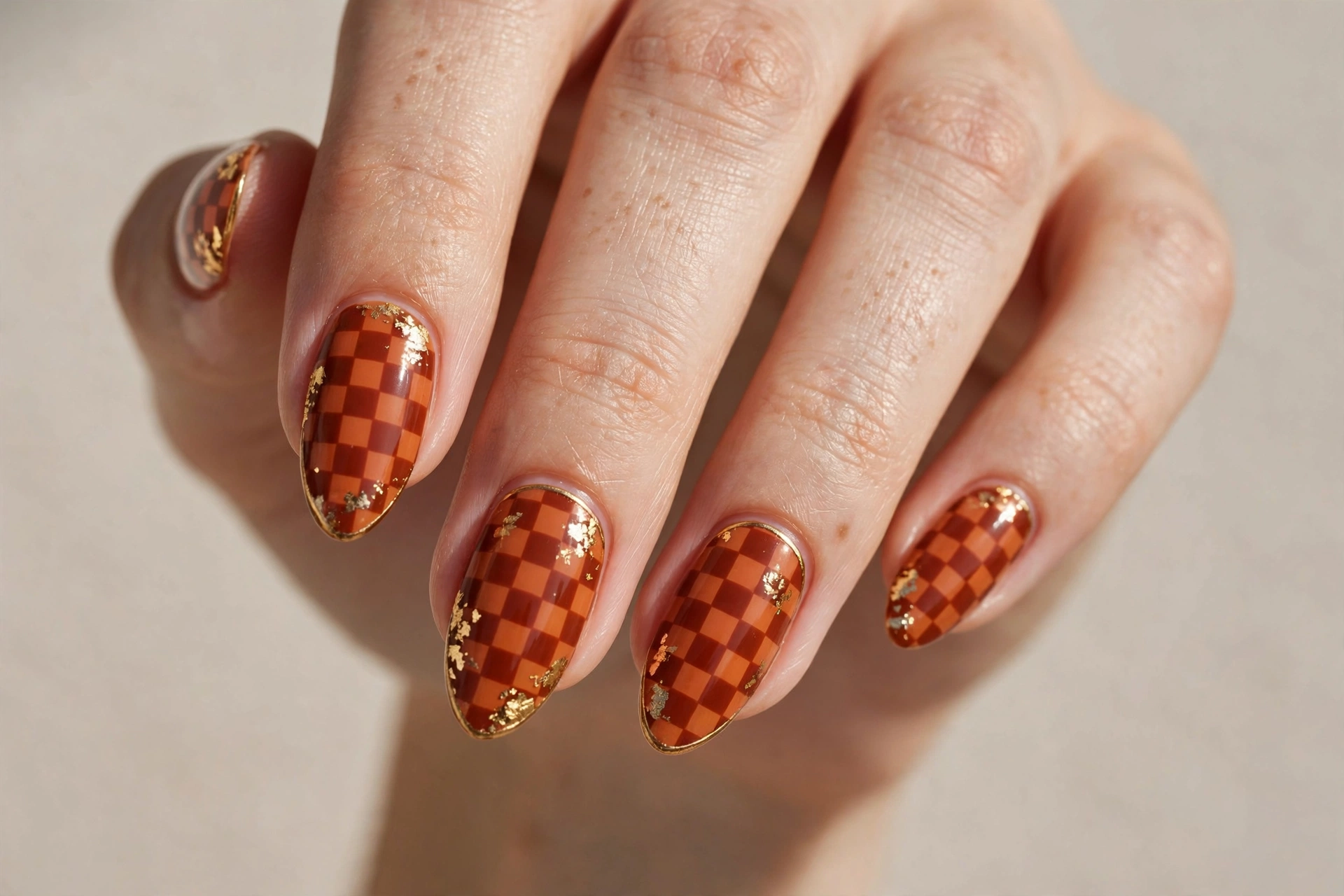 Burnt orange checkerboard nail art with gold accents on almond nails