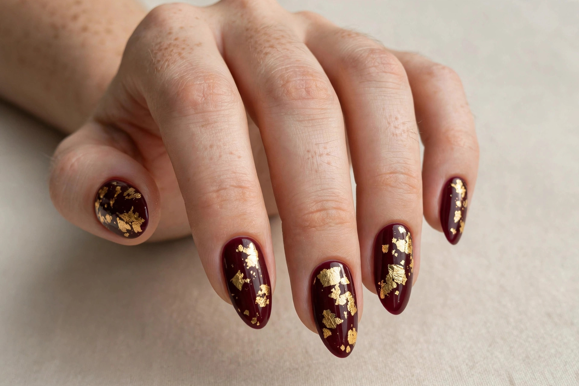Deep burgundy nails decorated with gold foil leaf flakes