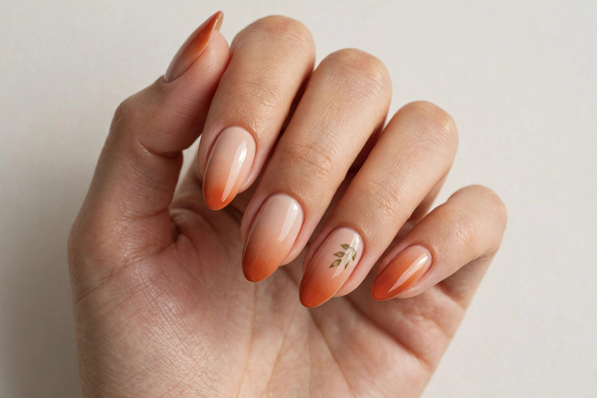 Ombré nails fading from nude to rust orange with a leaf accent nail