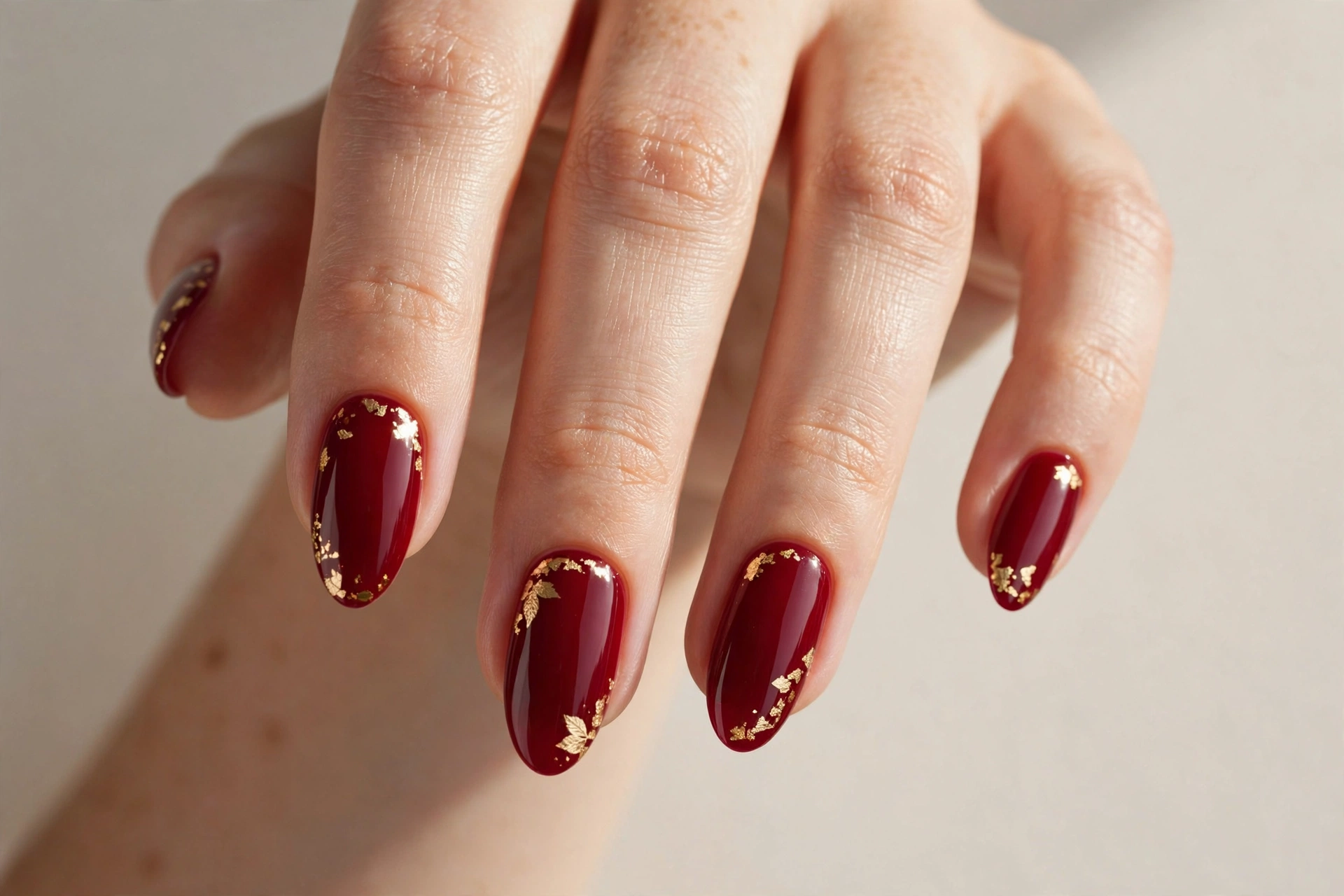 Cranberry red acrylic nails with hand-painted gold leaf accents