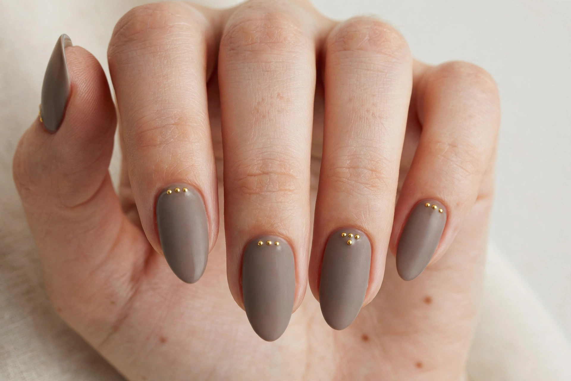 Warm taupe gray matte acrylic nails with small gold stud accents