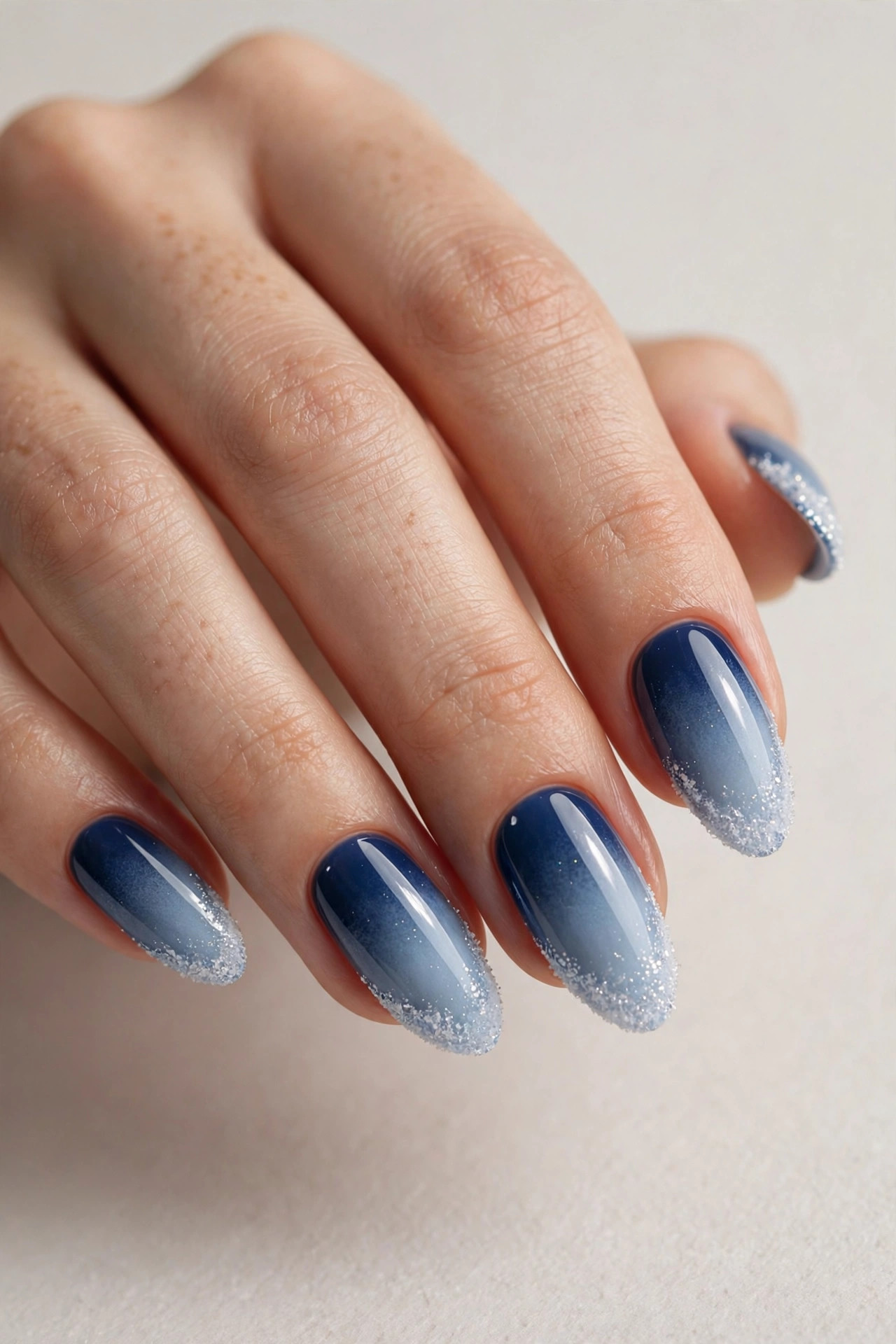 Frosty winter ombre gel nails fading from deep blue to white glitter tips