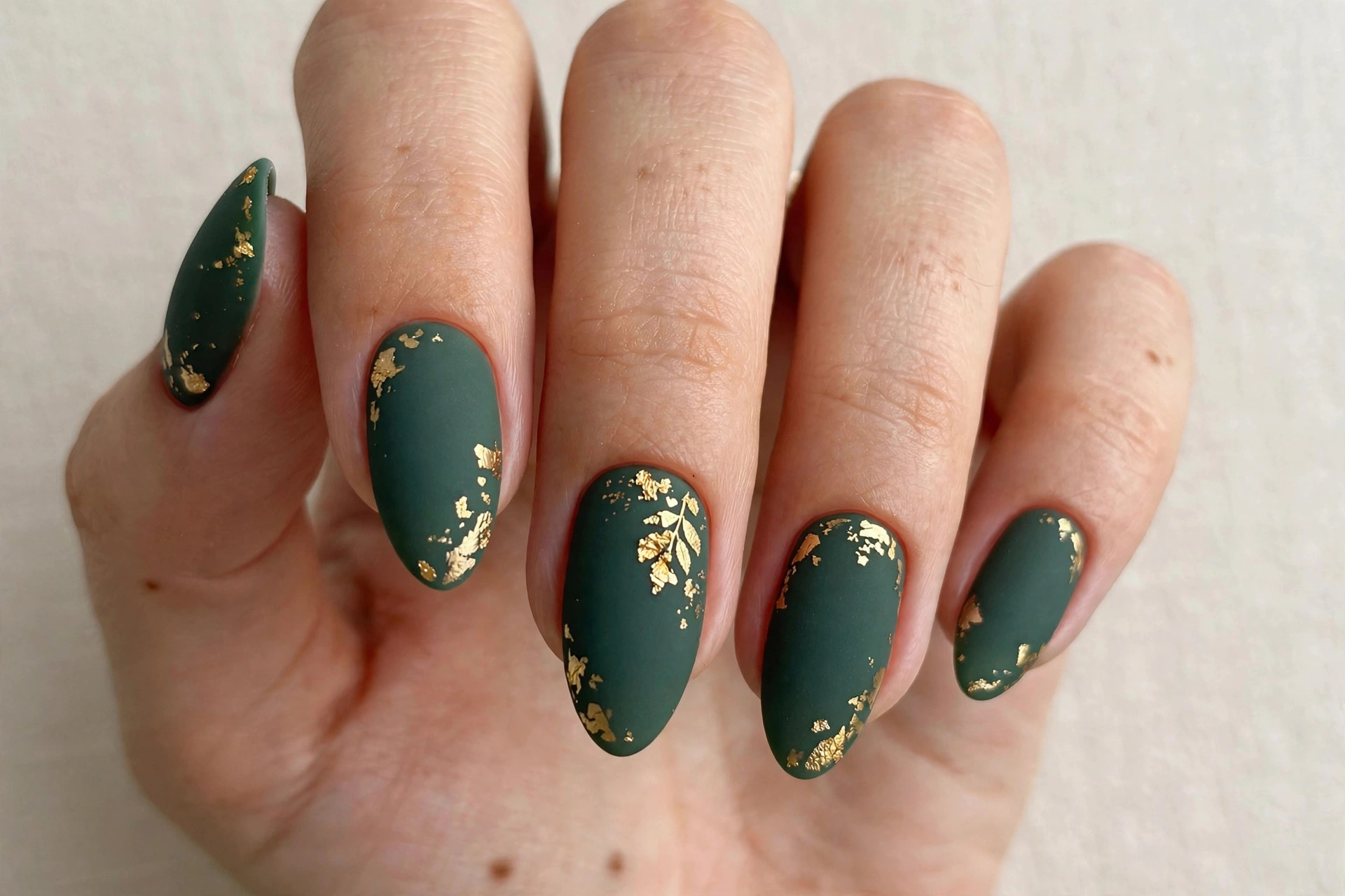 Matte forest green gel nails with delicate gold foil leaf accents