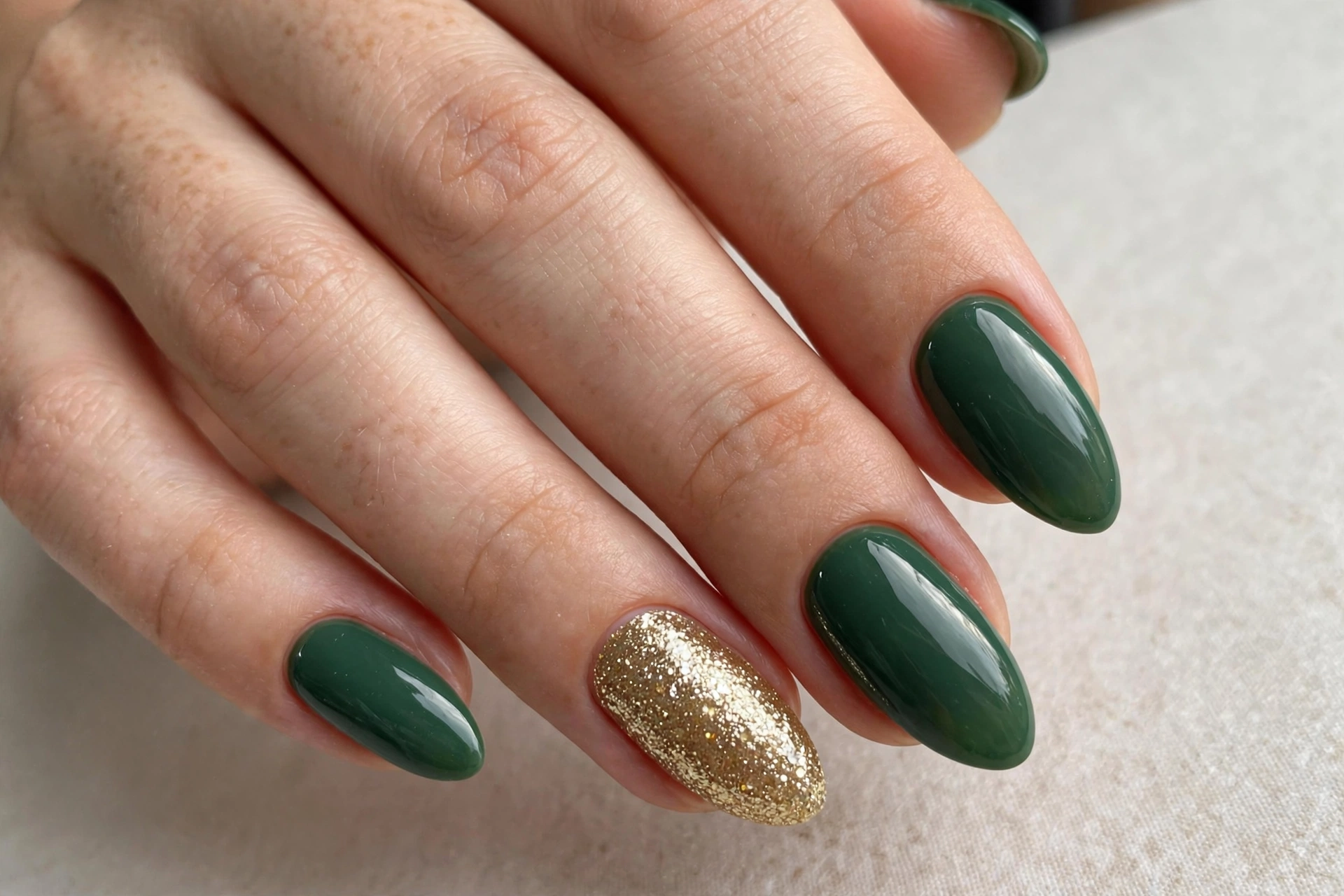 Close-up of forest green manicure with one sparkling gold glitter accent nail on almond shaped nails