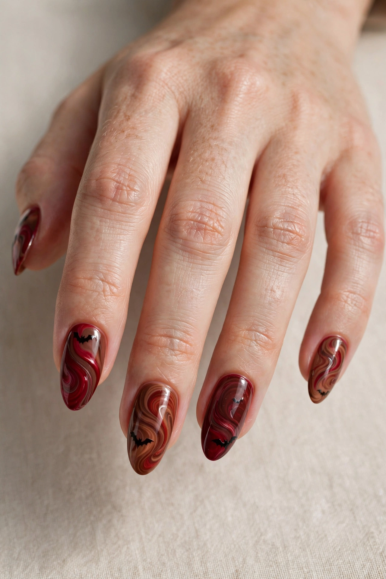 Deep red and warm brown swirled nail art with subtle bat silhouettes
