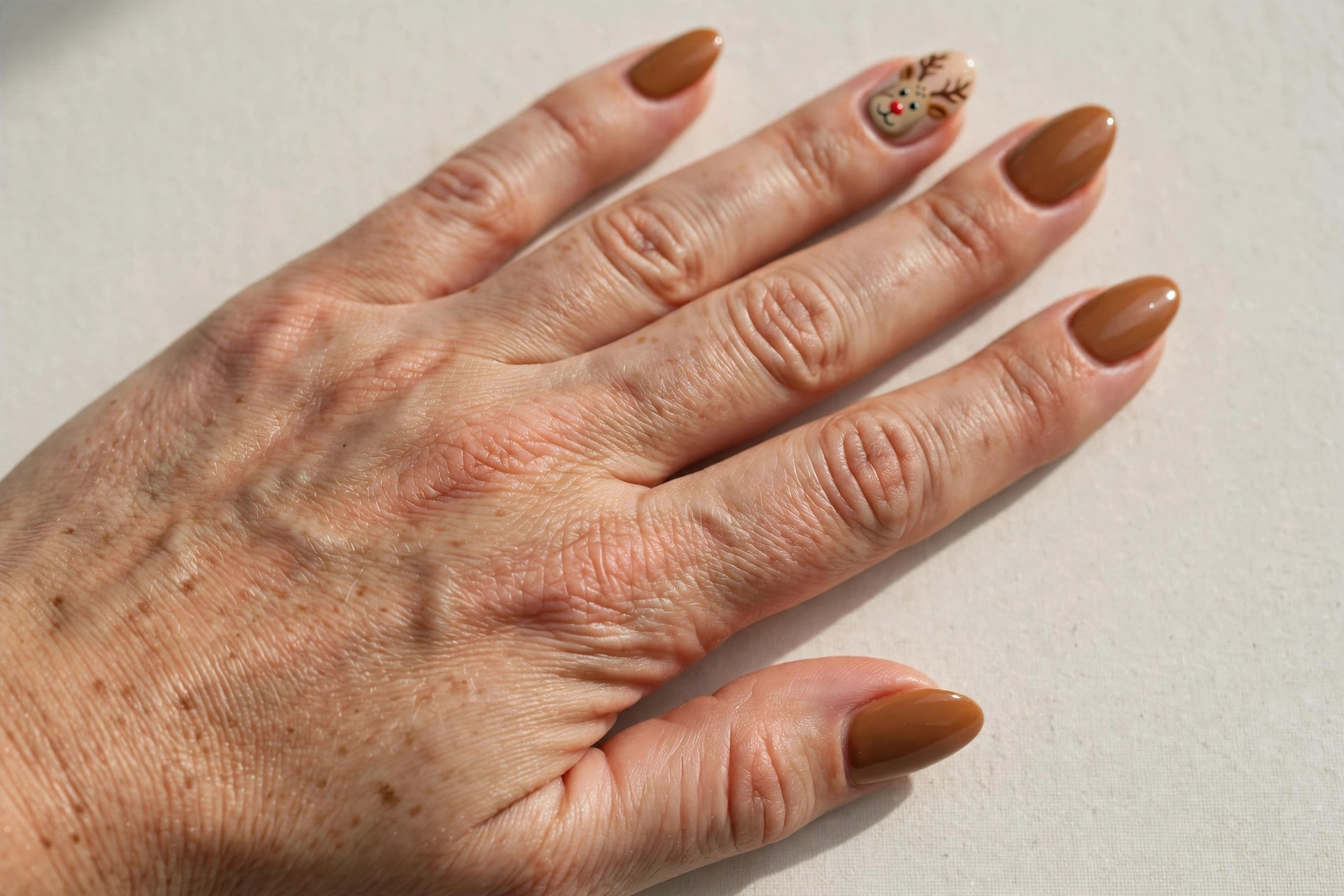 Caramel brown manicure with cute hand-painted reindeer face and red nose on accent nails