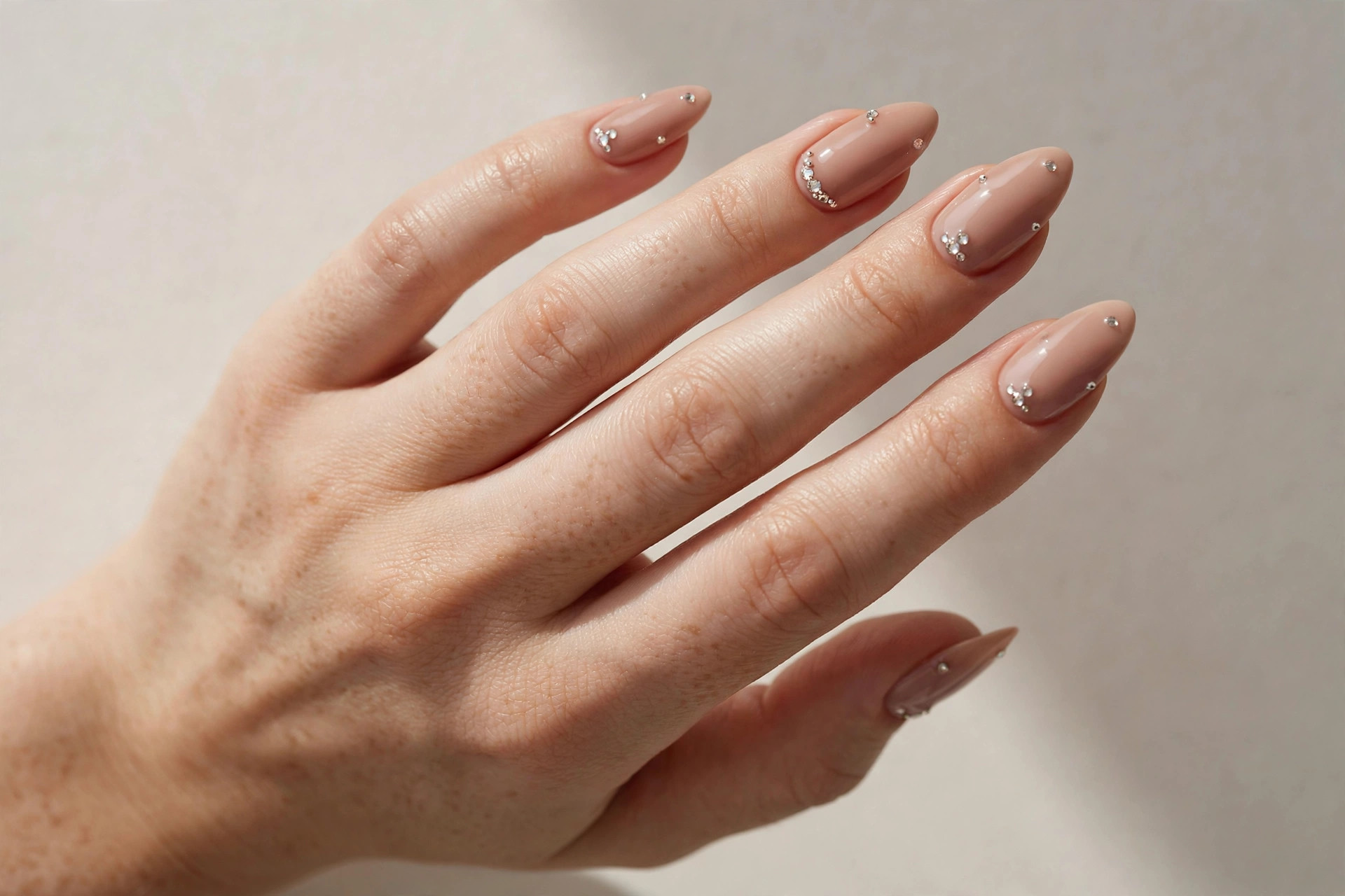 Nude manicure with small rhinestone embellishments on almond nails