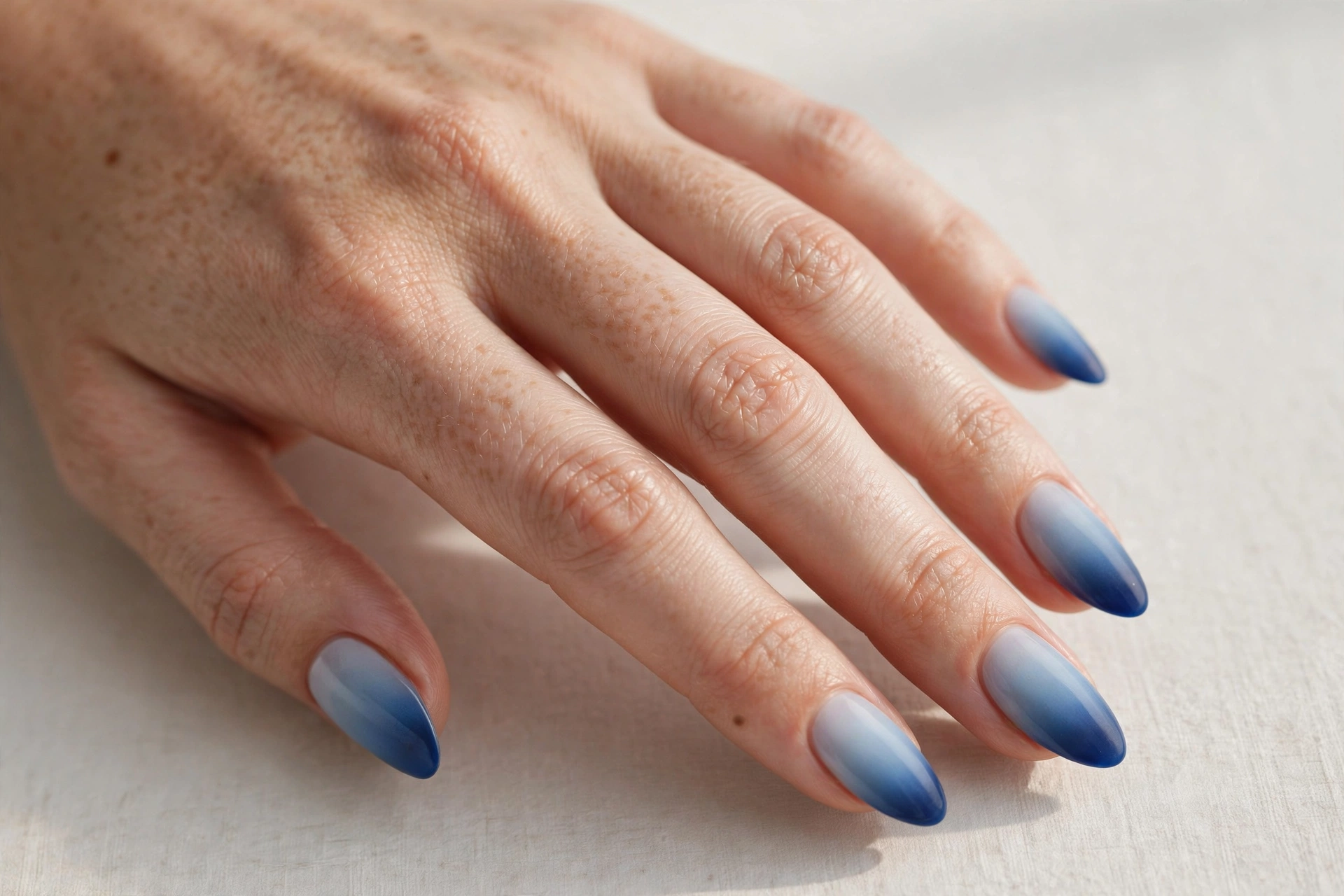 Close-up of a woman's hand with blue ombre gradient nails fading from pale to deep blue