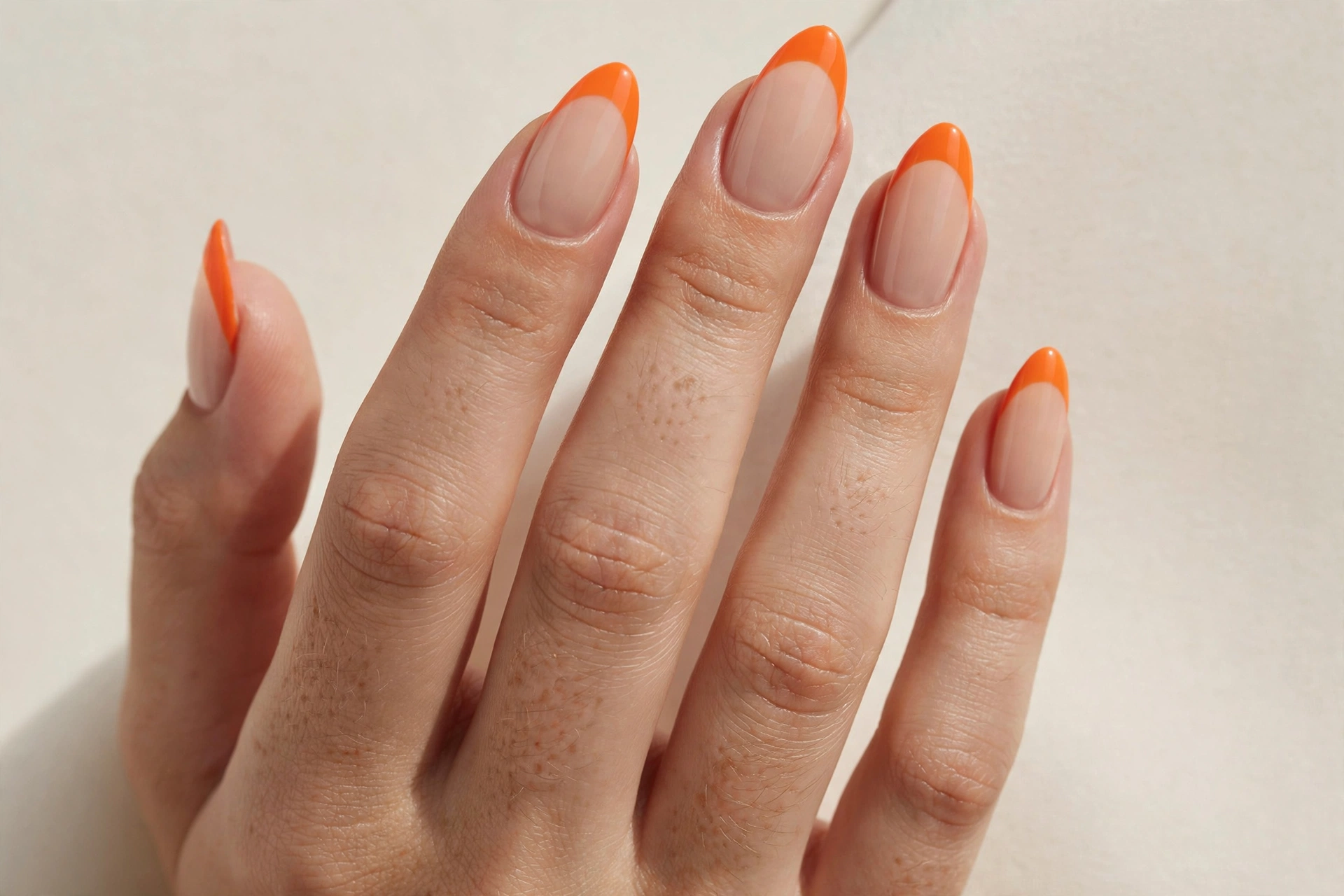 Orange french tip nails with nude base on almond shaped nails