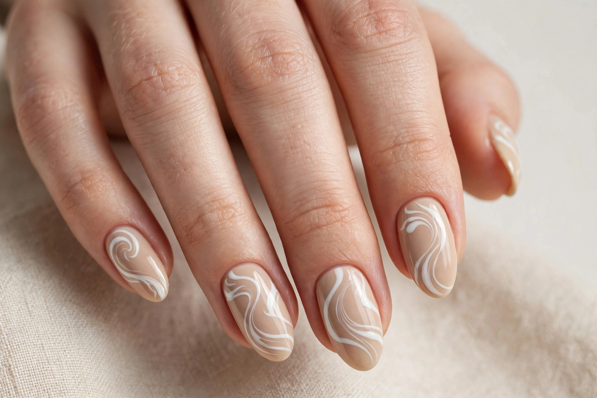 Close-up of latte beige nails with white swirl nail art on oval shaped nails