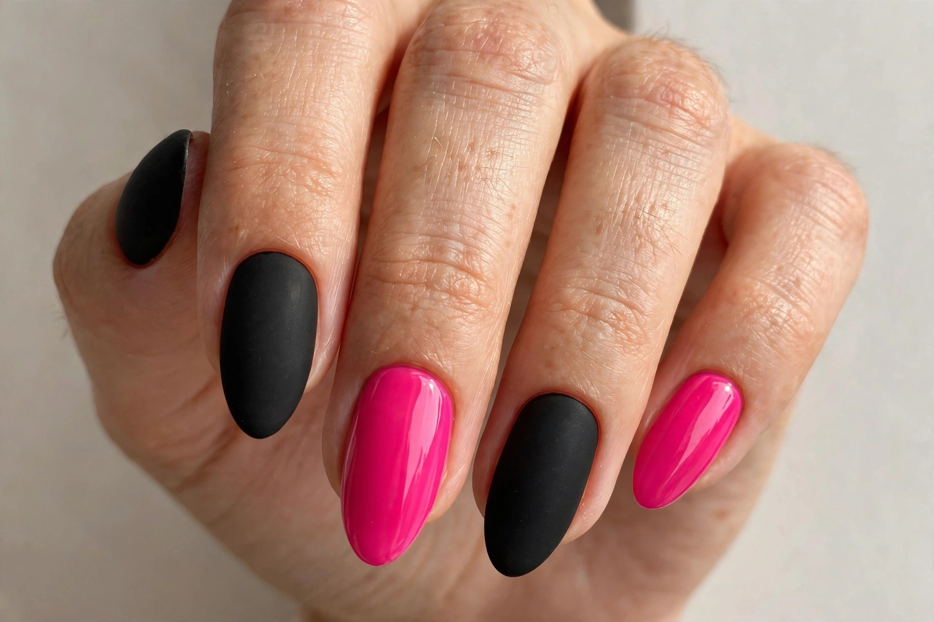 Matte black almond nails with two glossy hot pink accent nails