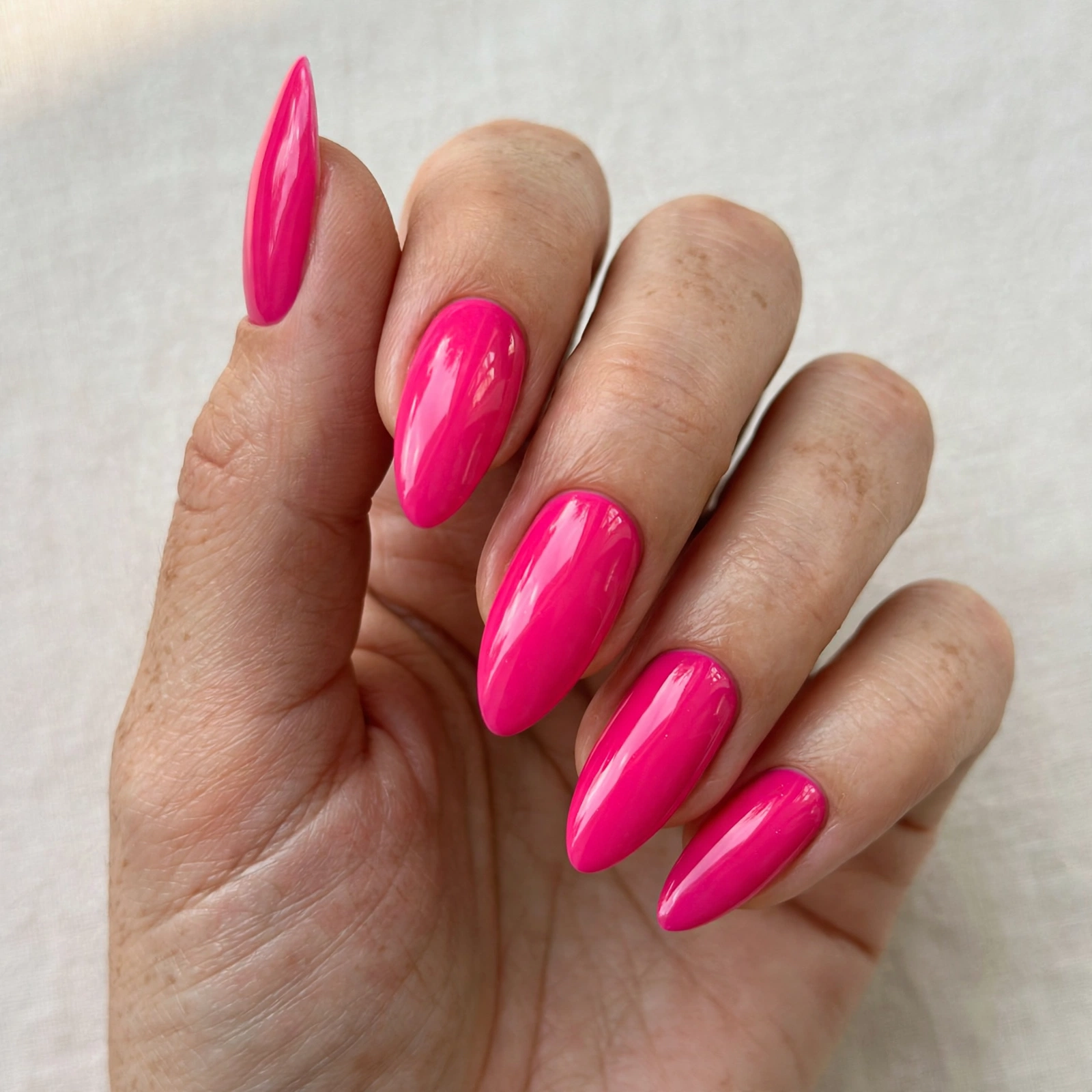 Close-up of a hot pink glossy manicure on long coffin-shaped nails