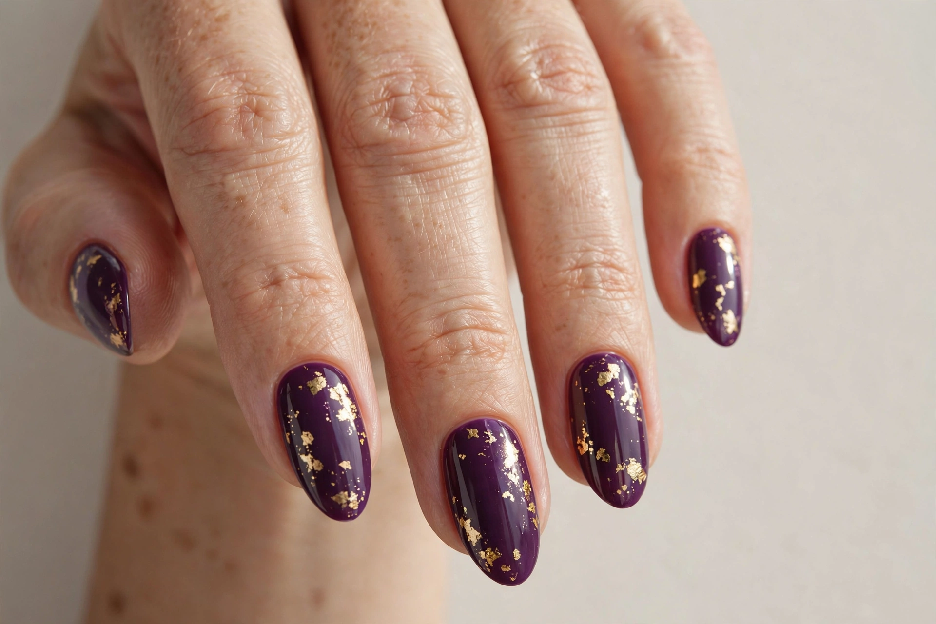 Deep plum nails with delicate gold foil flake accents