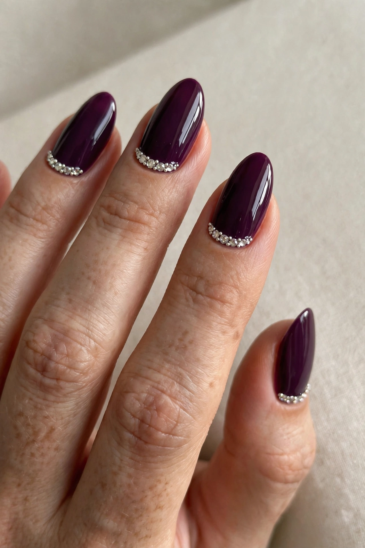 Deep plum nails decorated with sparkling rhinestone crystals along the cuticle