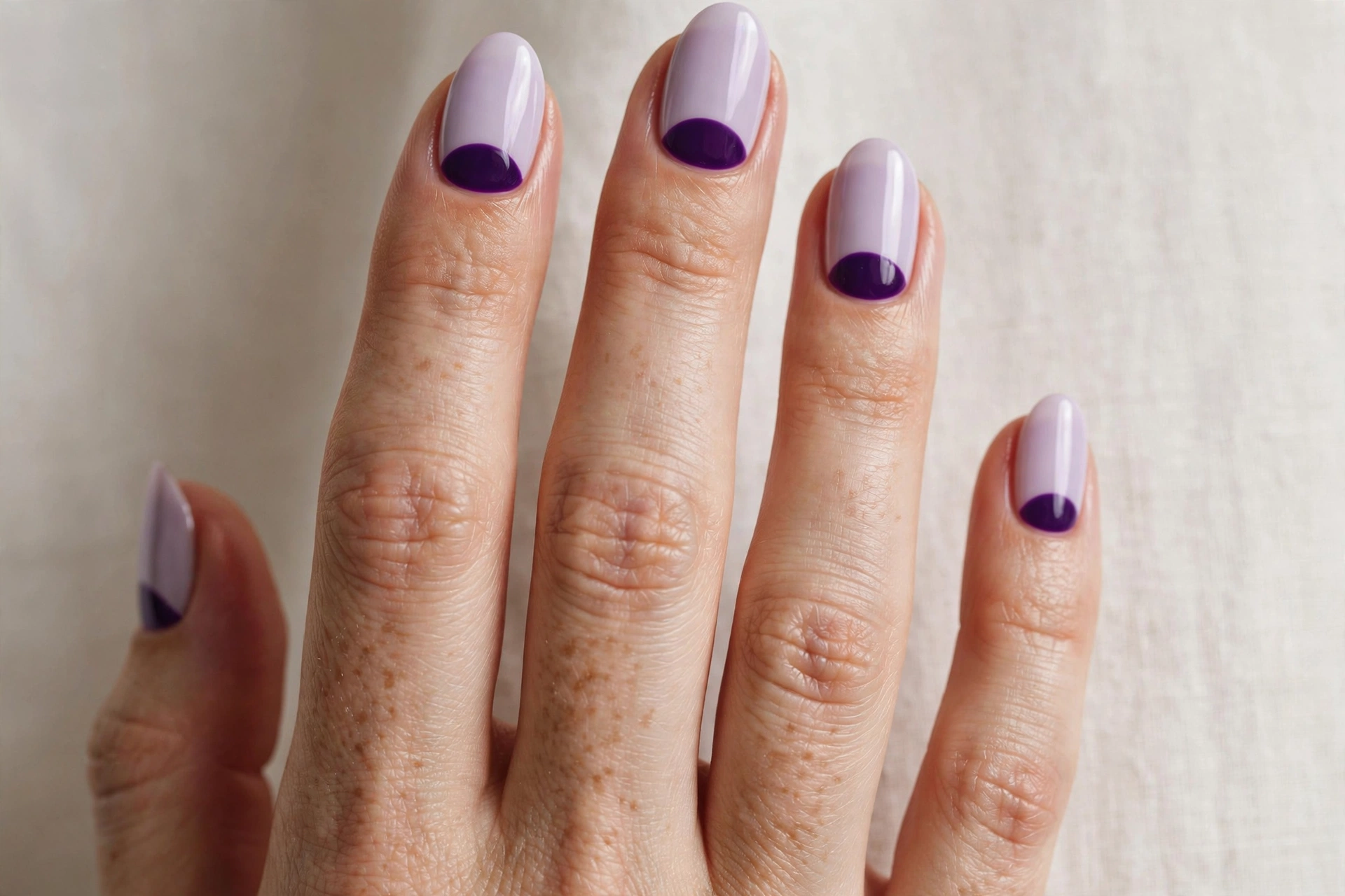Plum half-moon manicure with deep violet crescent at the cuticle over lilac base